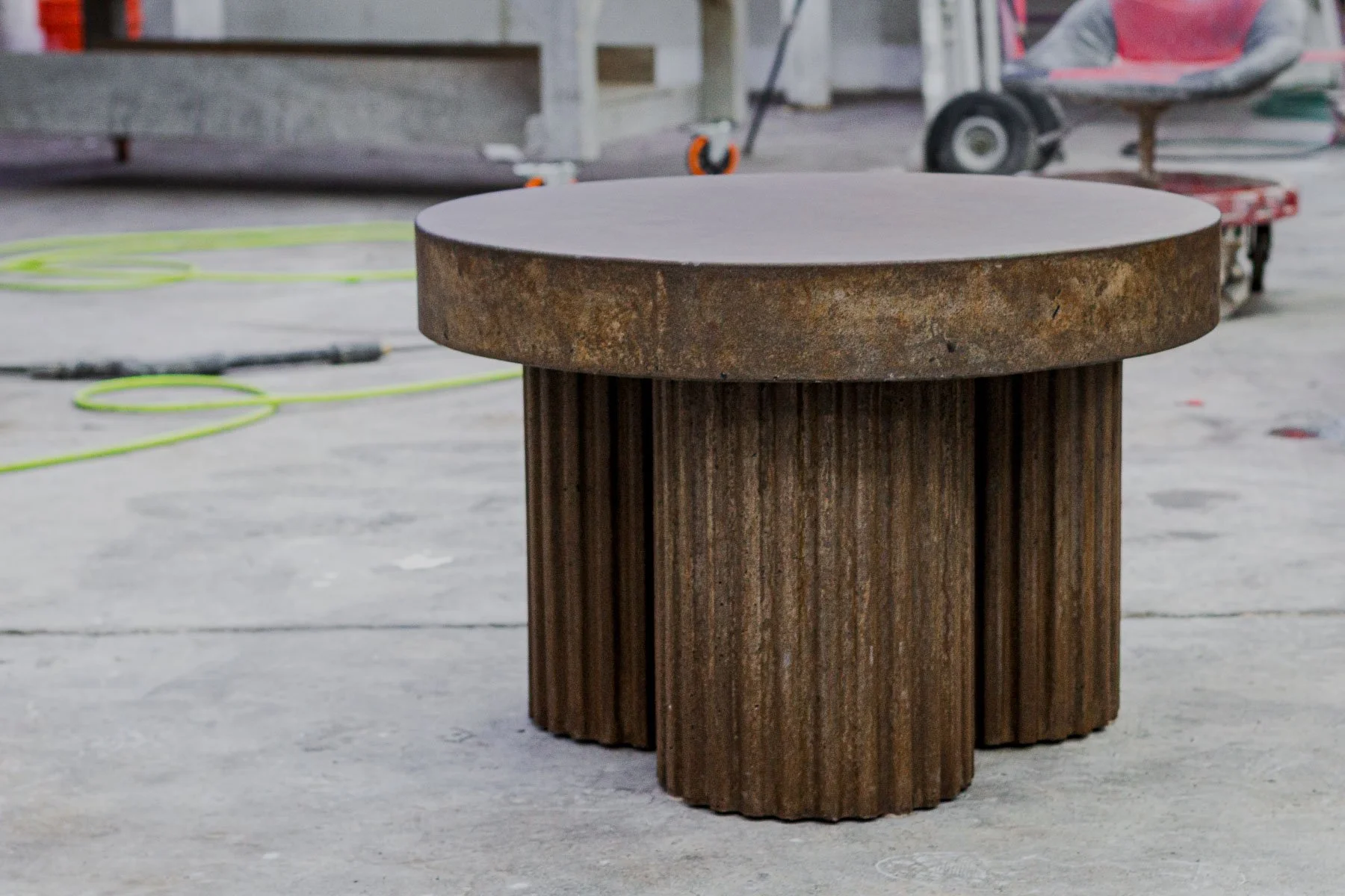 30" sculptural concrete coffee table photographed in studio, highlighting the deep fluted base and oxidized mineral surface variation.