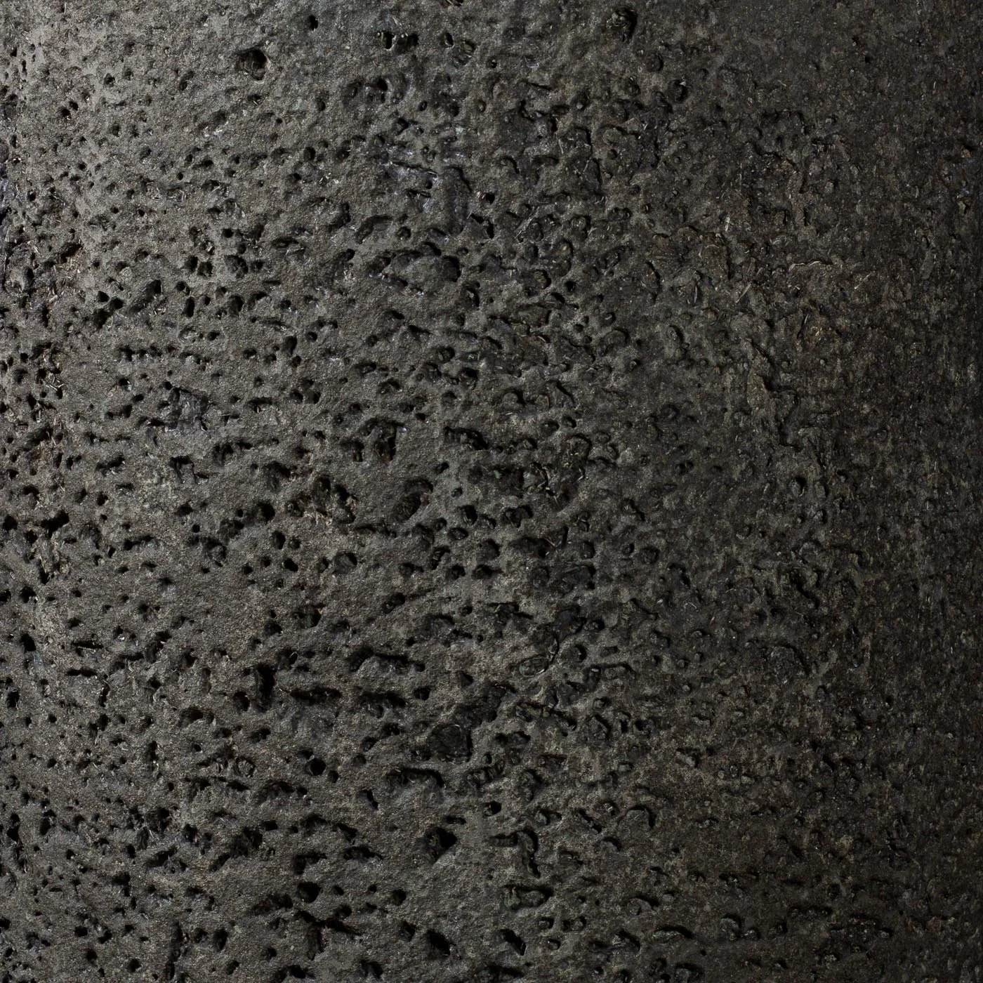 Close-up detail of eroded concrete surface showing dense pitting, mineral exposure, and cooled-lava texture development.