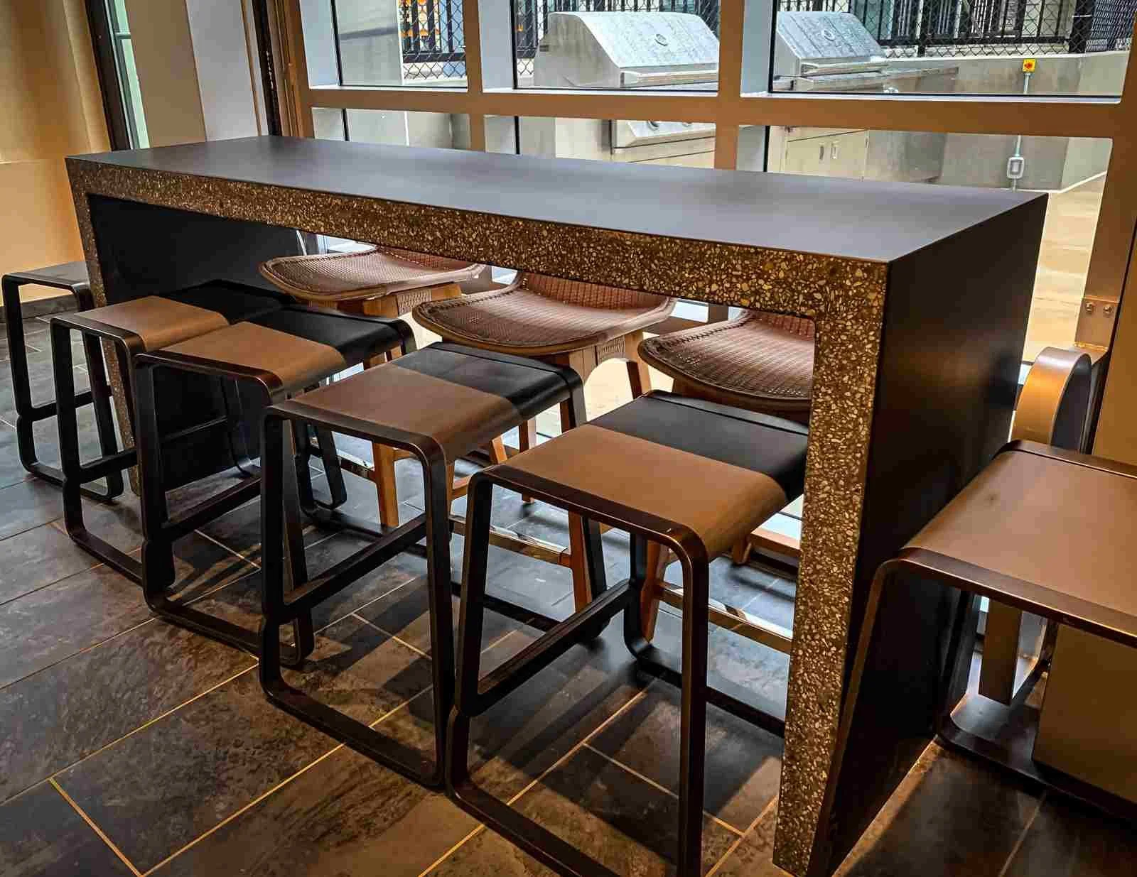 Custom concrete high table with exposed aggregate edge and monolithic form, designed and fabricated by The Concrete Anomaly for a commercial hospitality interior.