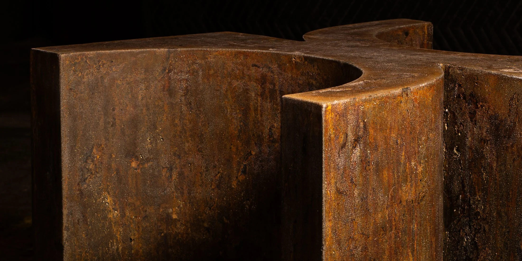 Close-up detail of a sculptural concrete furnishing by The Concrete Anomaly showing curved geometry, weathered corten-inspired texture, and monolithic edge thickness.