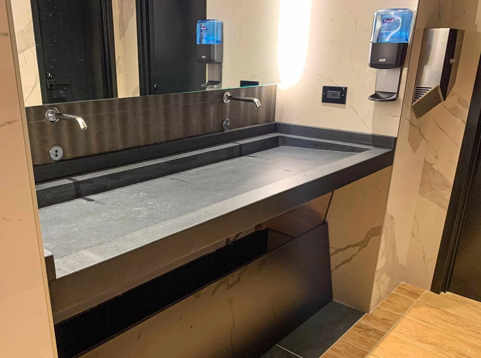 Custom cast concrete vanity countertop with integrated sink cutouts and wall-mounted fixtures in a commercial restroom setting.