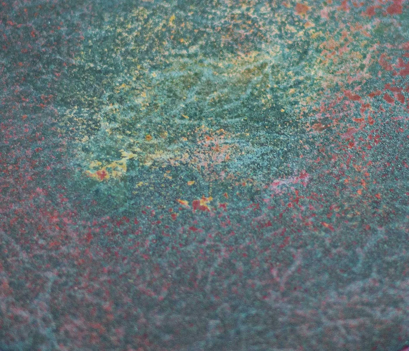 Close-up detail of oxidized concrete surface showing layered mineral pigment, abrasion, and weathered patina texture