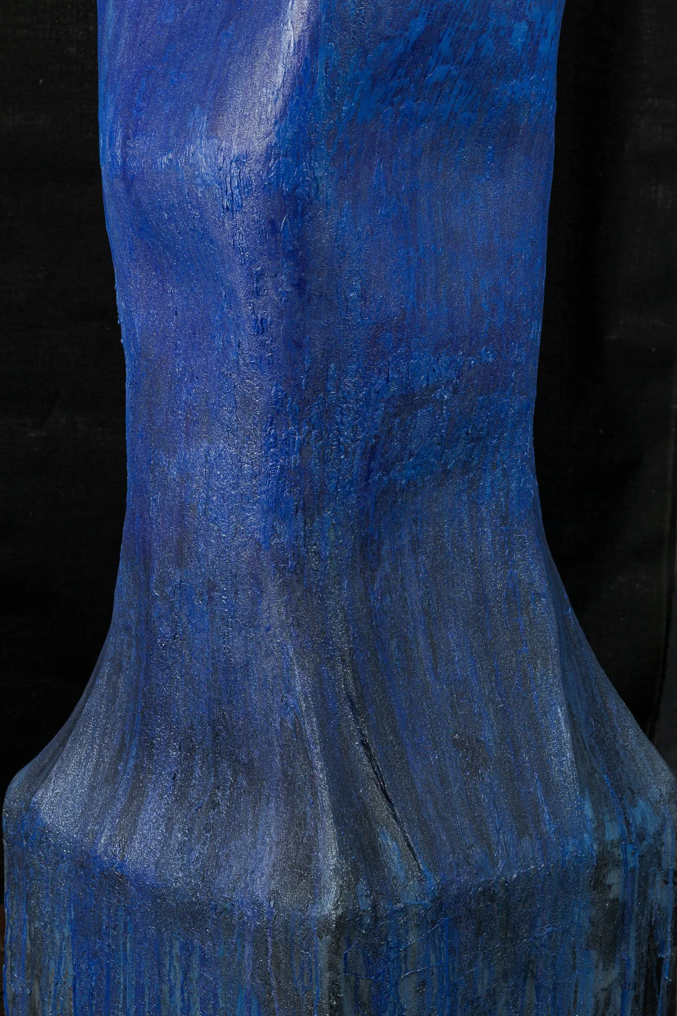 Close-up of a textured wooden sculpture painted in shades of blue, with a dark background.
