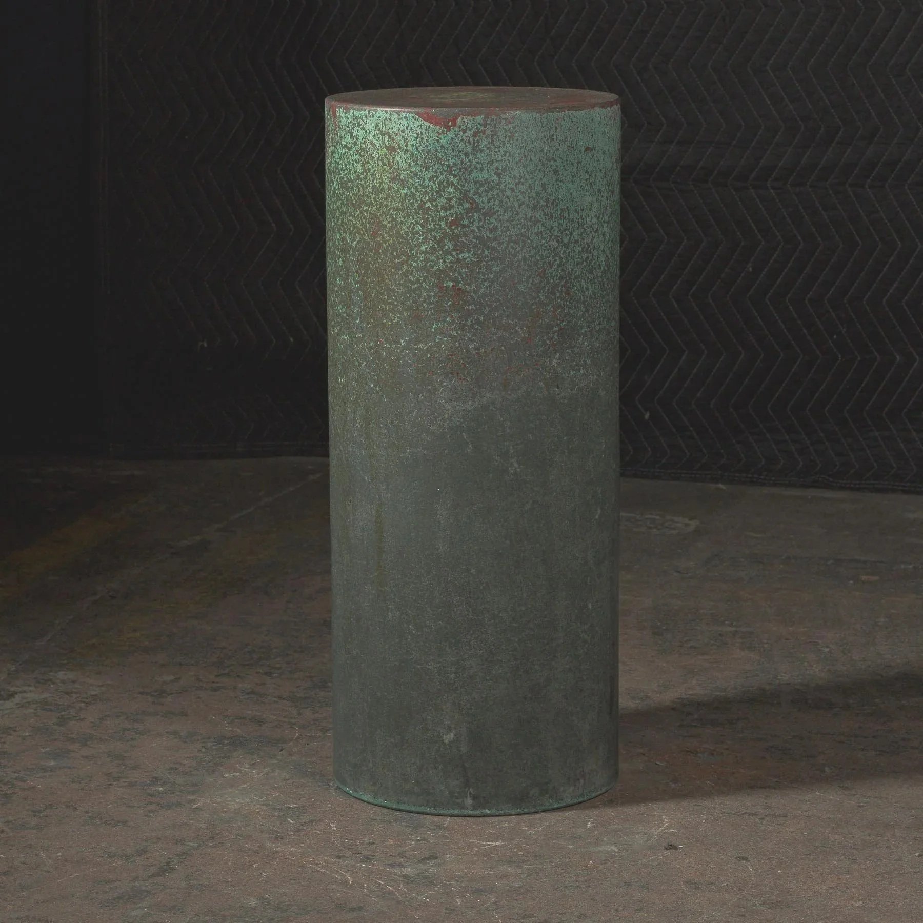 Hand-cast GFRC concrete cylinder with weathered green oxidation, subtle copper undertones, and atmospheric industrial surface variation.