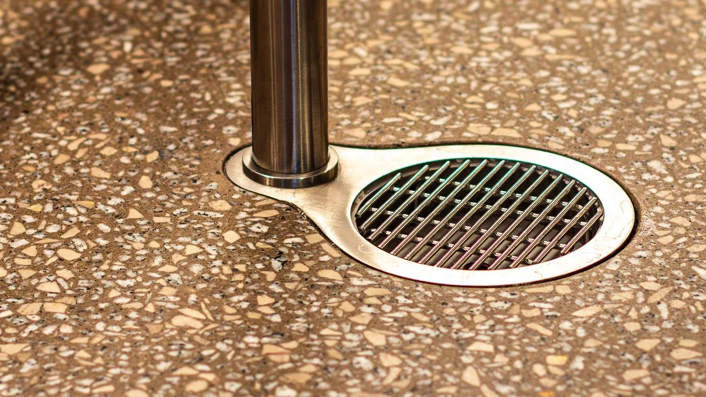 Completed custom integrated terrazzo floor drain installation featuring polished aggregate concrete finishing around a premium plumbing fixture at an entry threshold.
