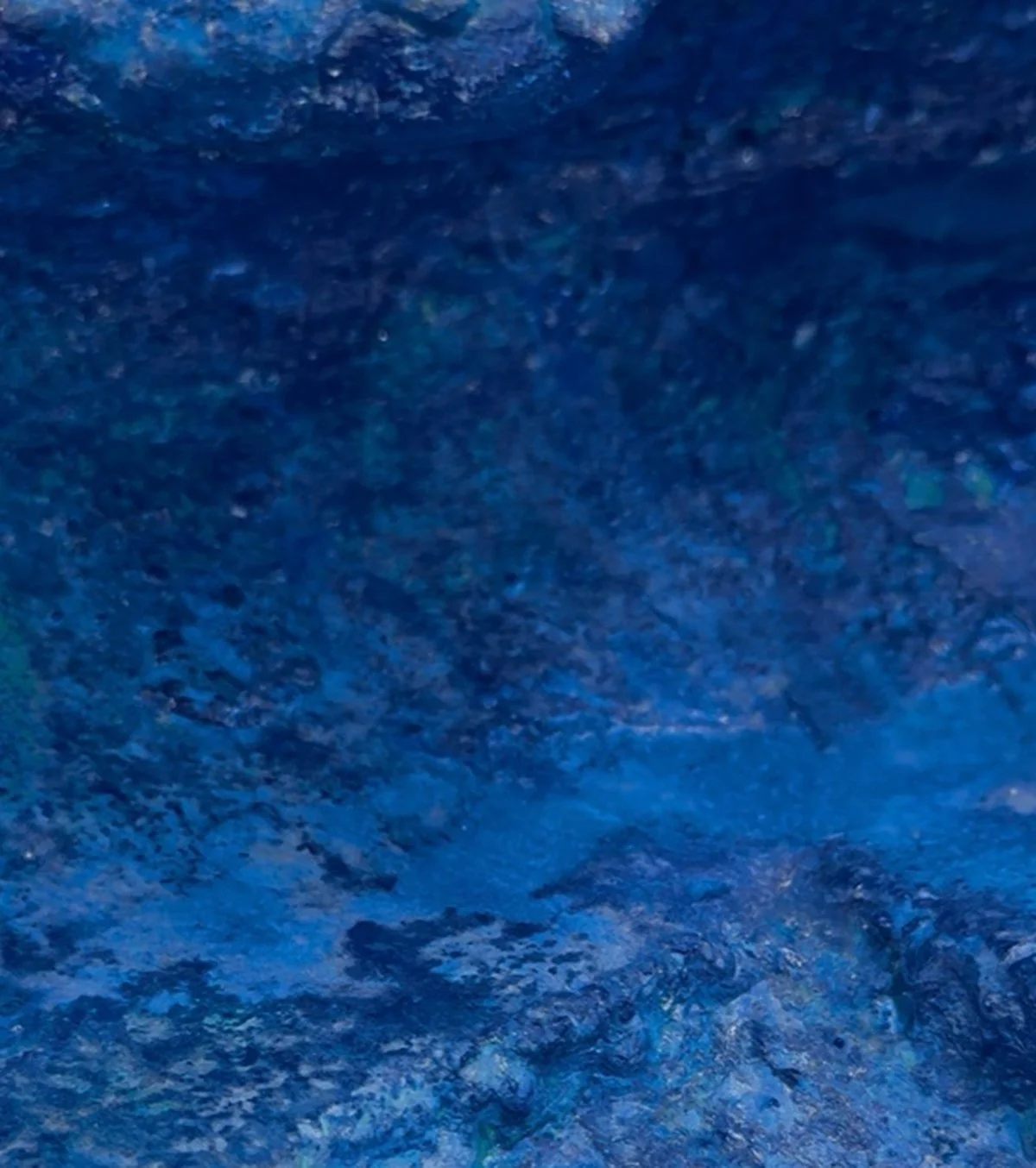 Close-up of a blue textured surface, possibly fabric or paper, with variations in color and pattern.