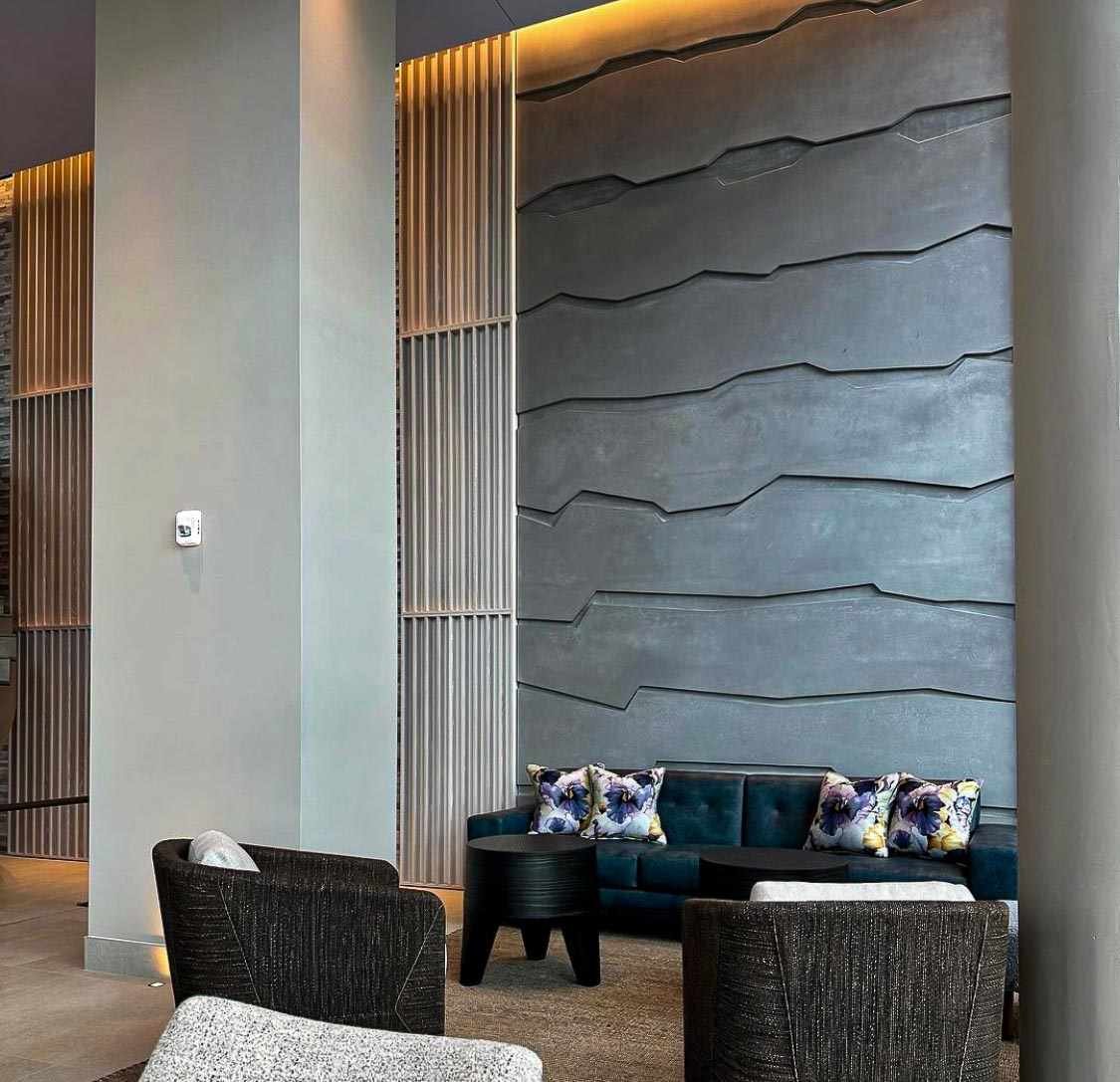 Custom cast concrete wall panels with layered relief texture installed within a hotel lobby seating area.