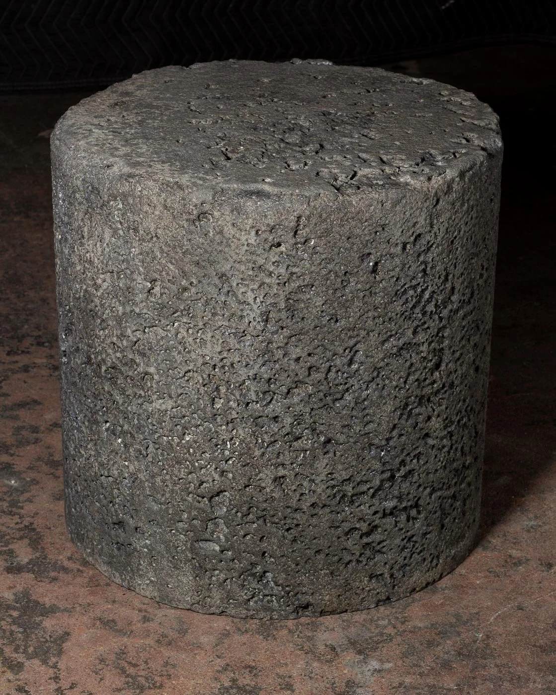 Cast concrete side table featuring heavily distressed lava-like texture with exposed mineral variation and softened cylindrical geometry.