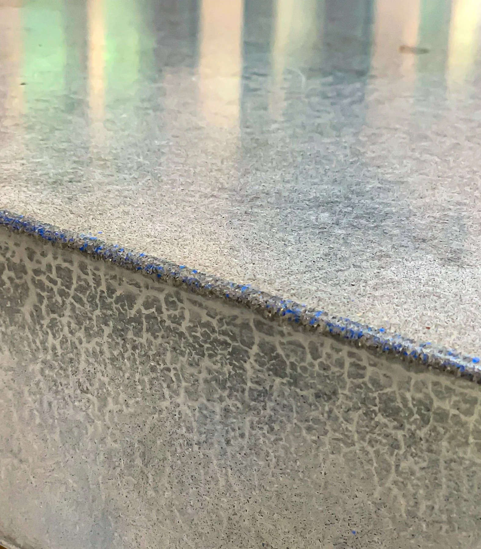 Close-up detail of honed salt and pepper concrete edge with electric blue mineral infusion and reflected light condition.