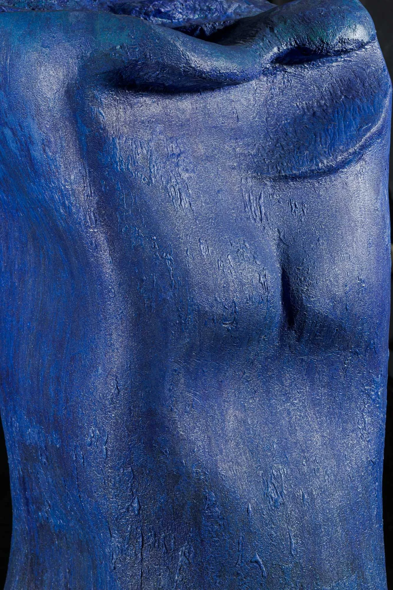 Close-up of a blue painted sculpture of a human torso, highlighting the textured surface and contours.