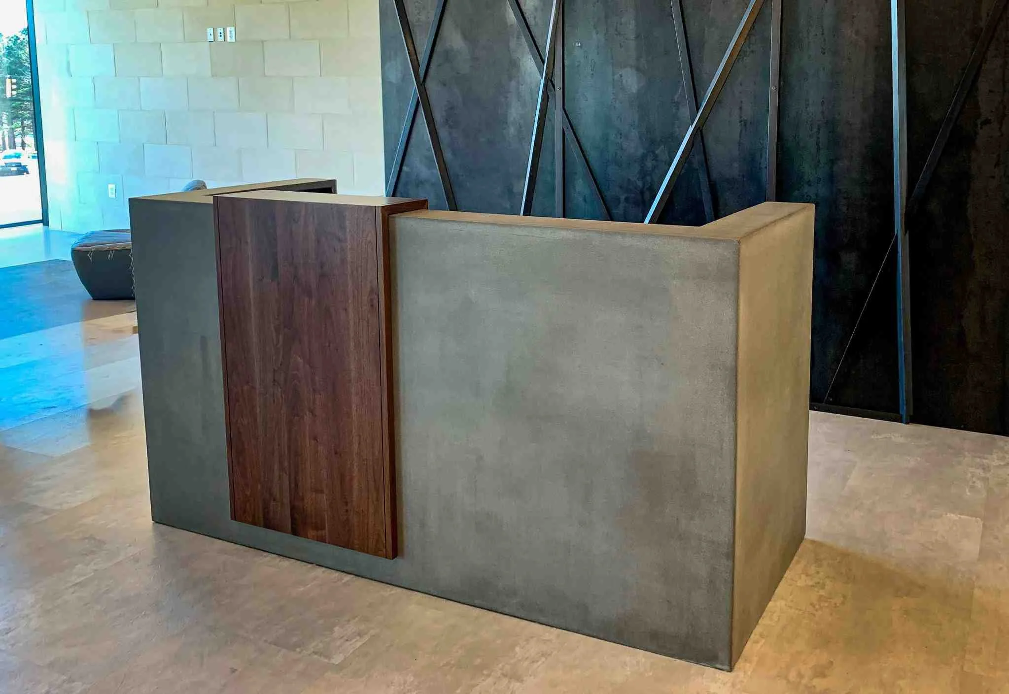 Custom reception desk fabricated with monolithic concrete panels, integrated wood accent surfaces, and textile backing, forming a sculptural front-of-house element within a modern lobby.