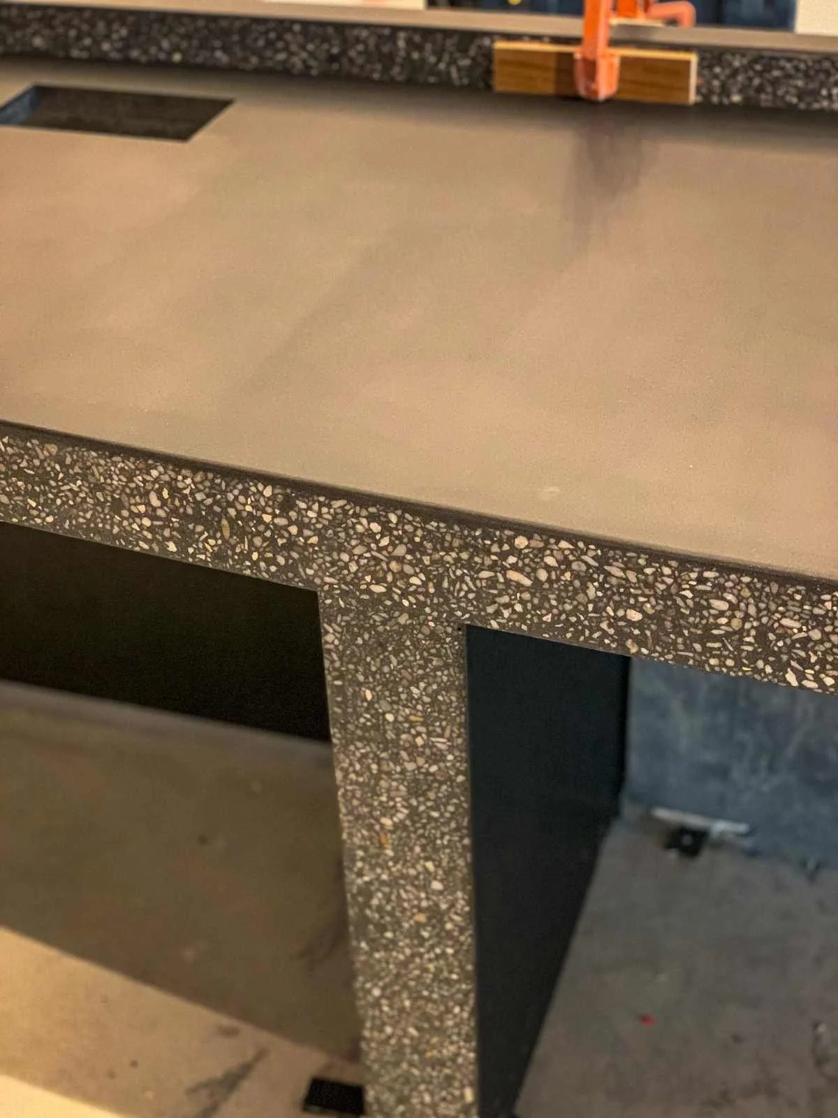 Close-up detail of a custom turnkey concrete desk showing honed work surface and exposed aggregate edge, fabricated by The Concrete Anomaly.