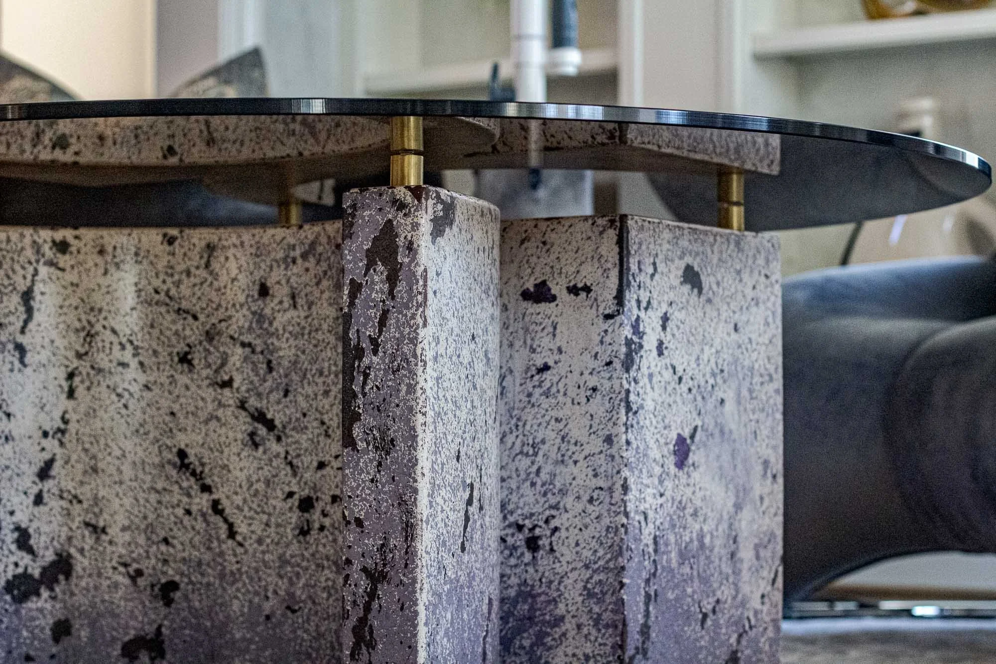 Detail of a sculptural concrete table with textured curved supports, brass spacers and a dark tabletop by The Concrete Anomaly
