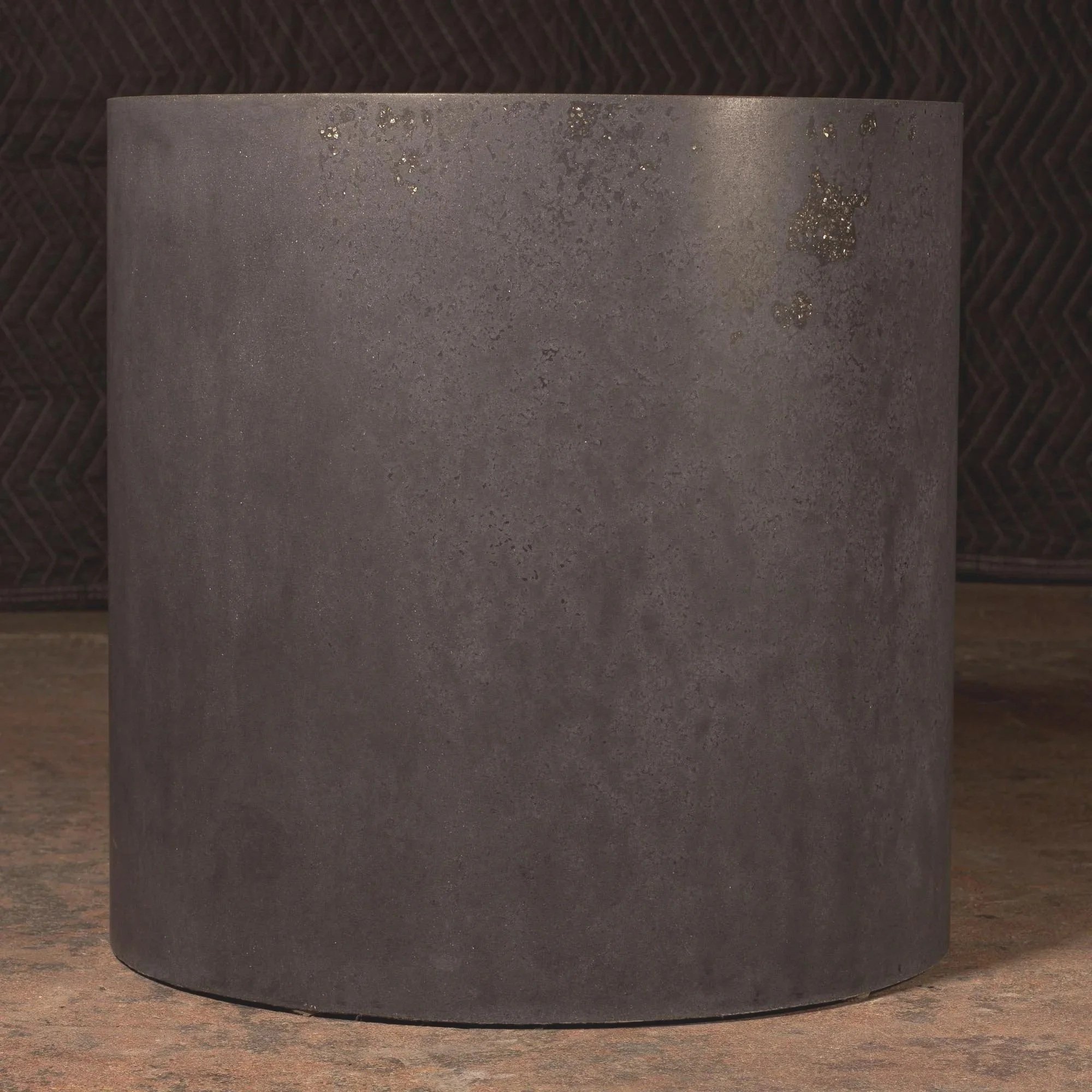 Hand-cast GFRC concrete cylinder with deep charcoal pigment, quiet surface variation, and embedded mineral accents throughout the form.