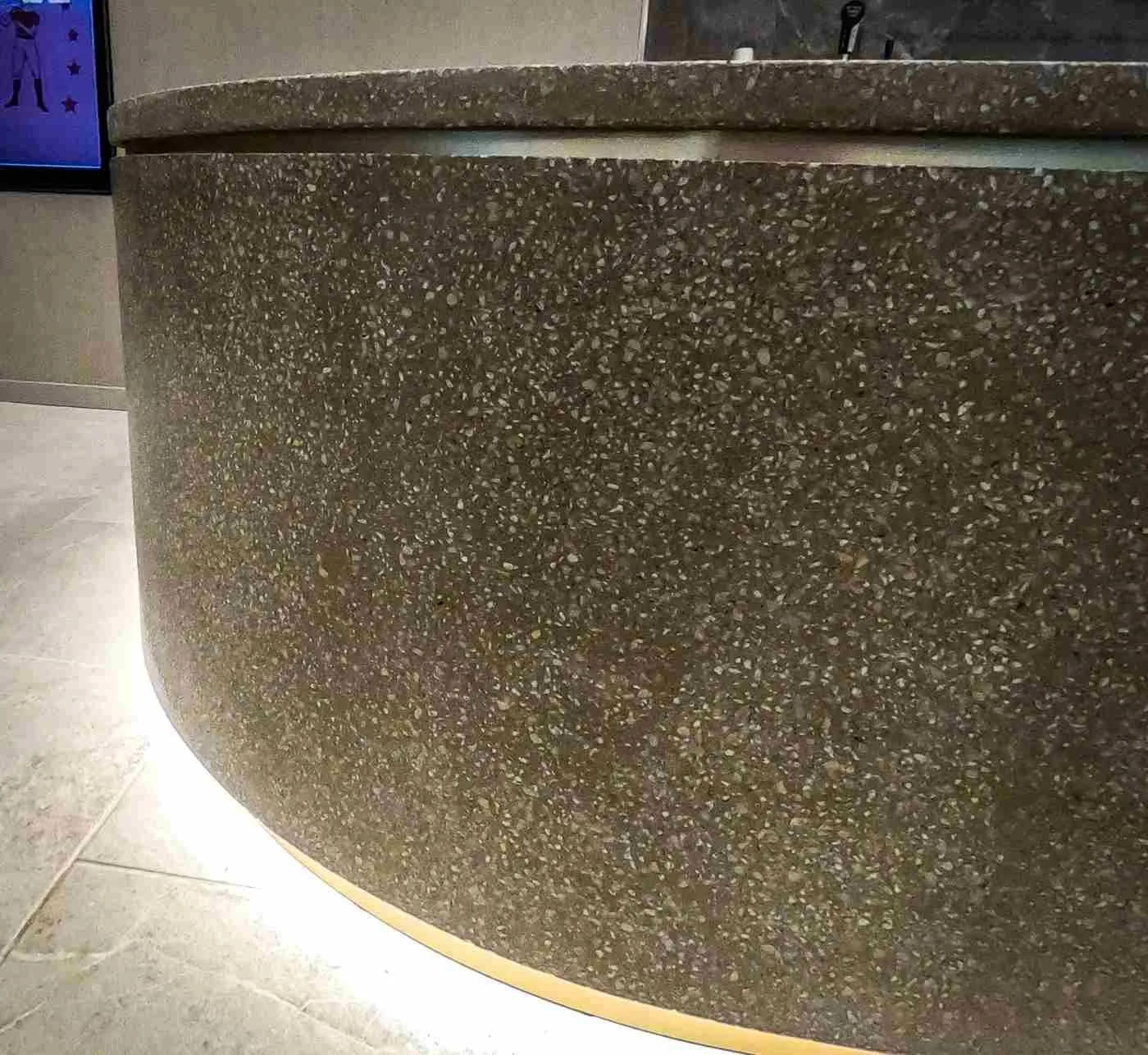 Curved custom cast concrete reception desk with exposed aggregate finish and integrated base lighting in a commercial interior.