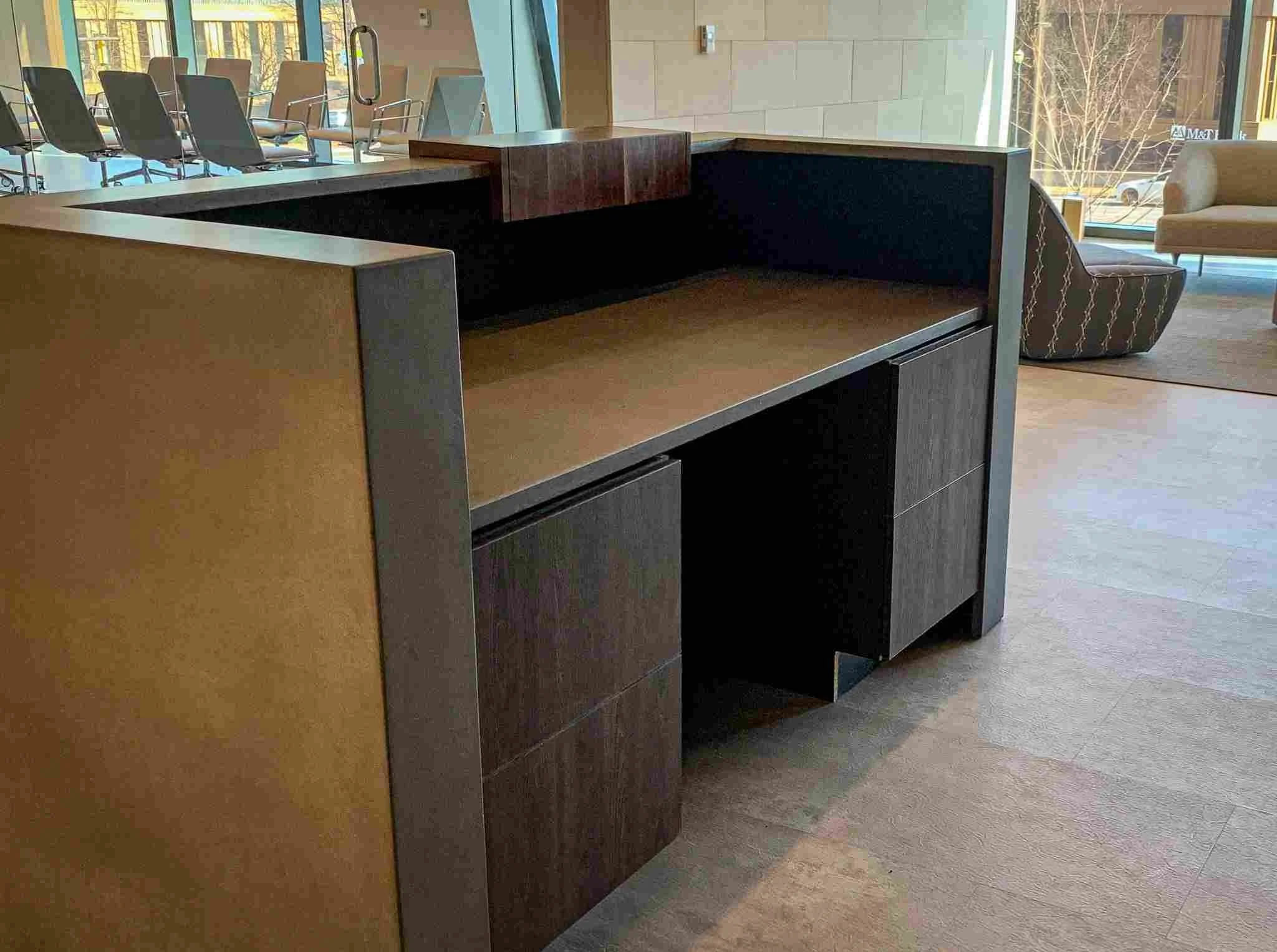 Modern office waiting area featuring a custom wood and concrete reception desk, expansive glazing for natural light, and curated seating arranged to complement the architectural material palette.