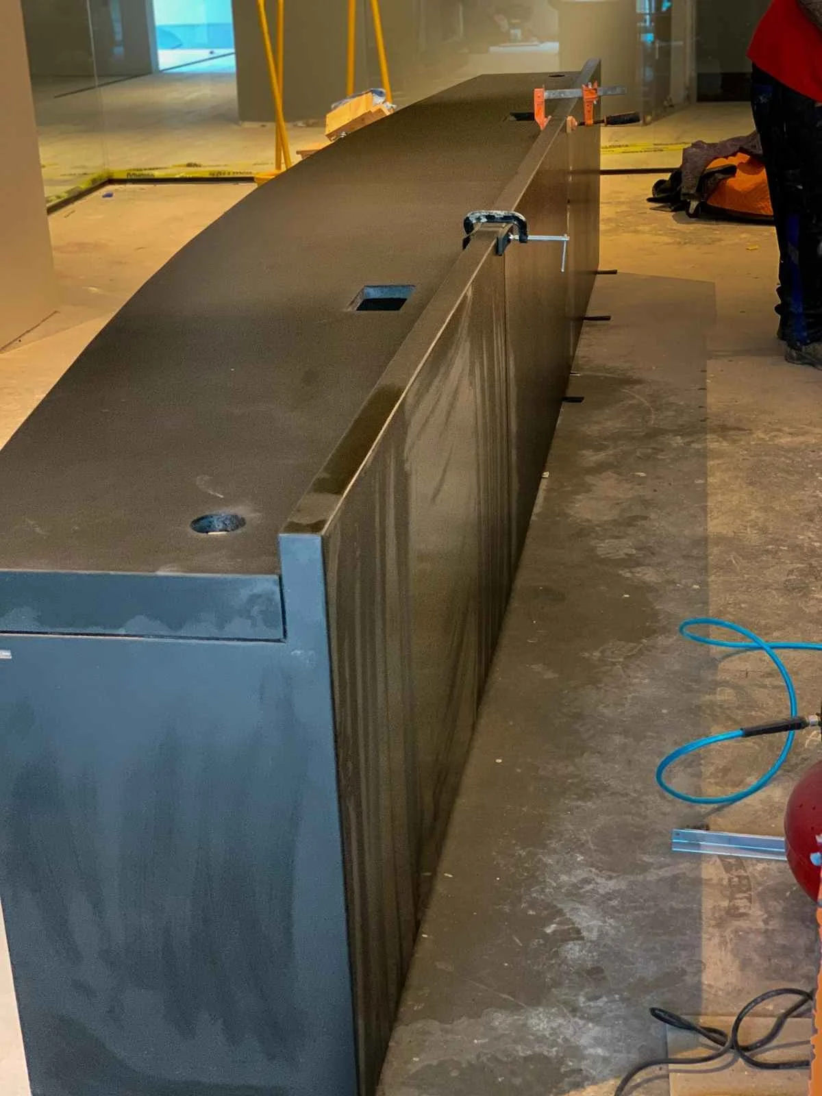 Installed base section of a custom turnkey concrete desk with honed surface and integrated cable pass-throughs, fabricated by The Concrete Anomaly.