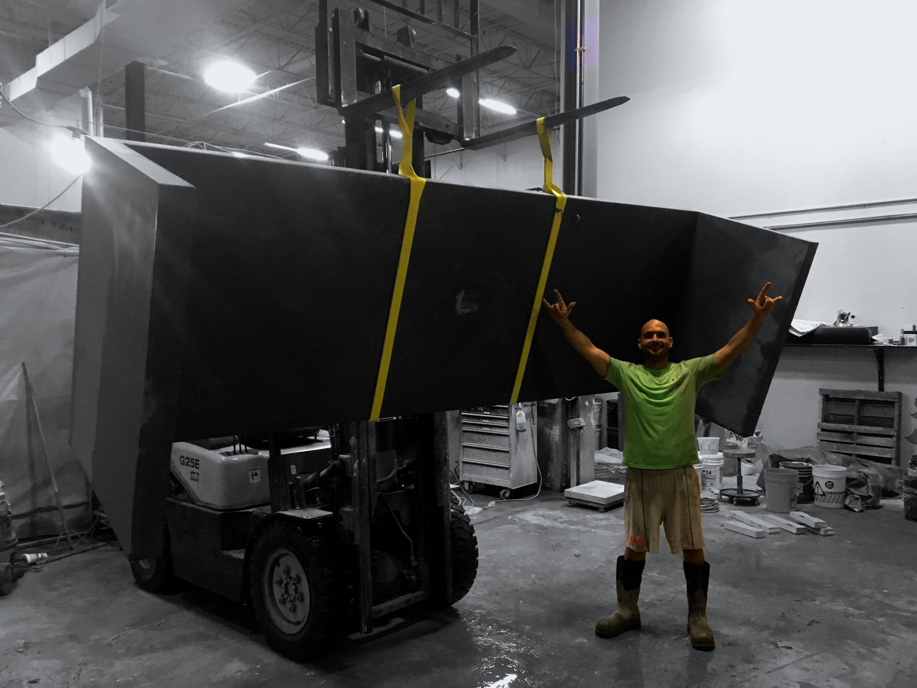 Black and white photograph of a forklift lifting a massive concrete slab inside a working concrete studio, emphasizing industrial scale and craftsmanship.