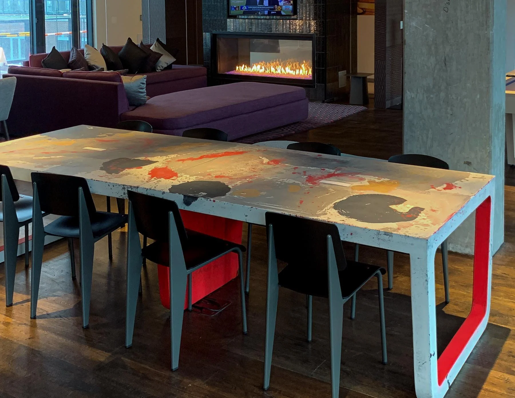 Custom architectural concrete community table with integrated color fields and monolithic leg structure installed within a hospitality lounge environment.