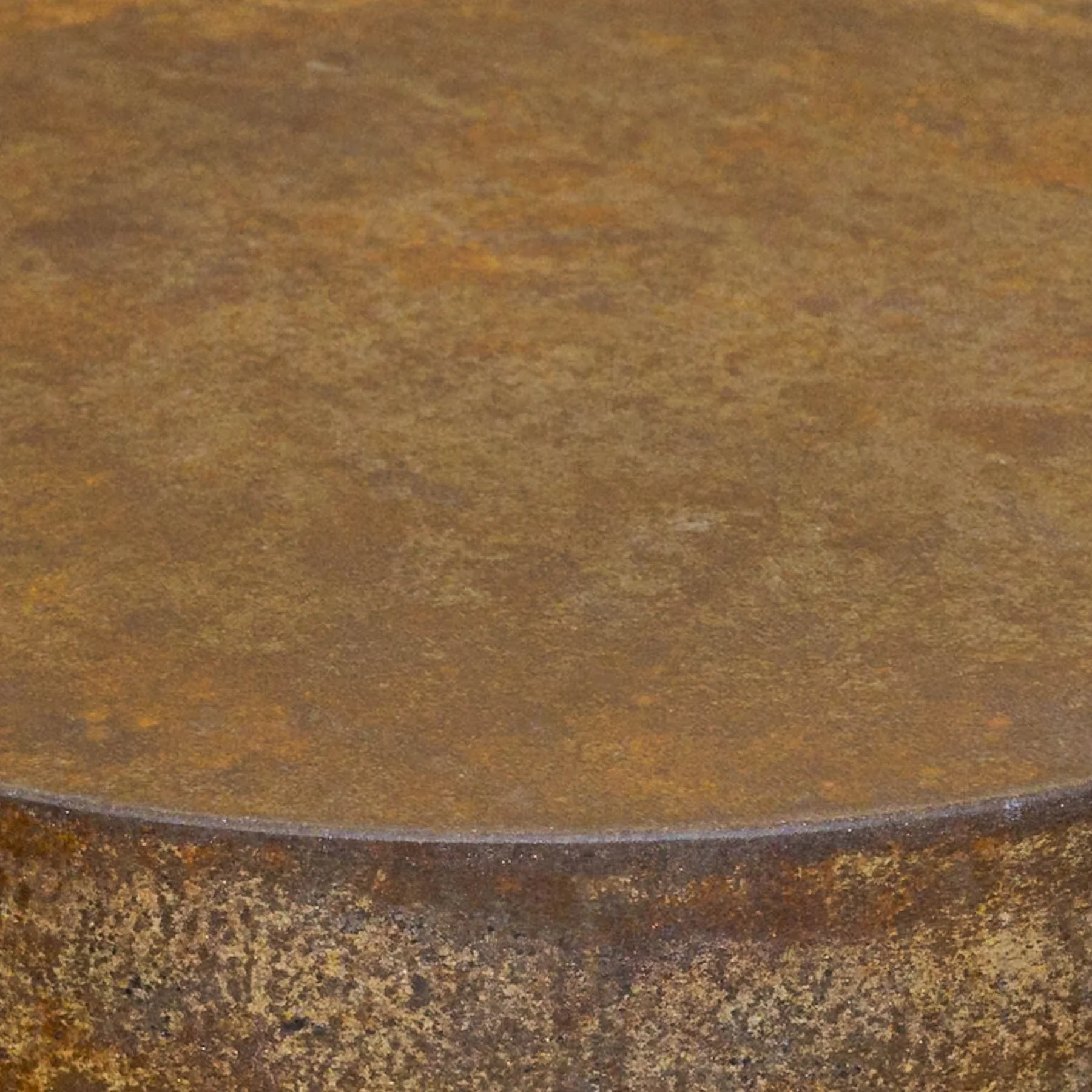 Close-up detail of a weathered concrete surface featuring warm tobacco tones, subtle oxidation, and layered mineral texture along a rounded edge.