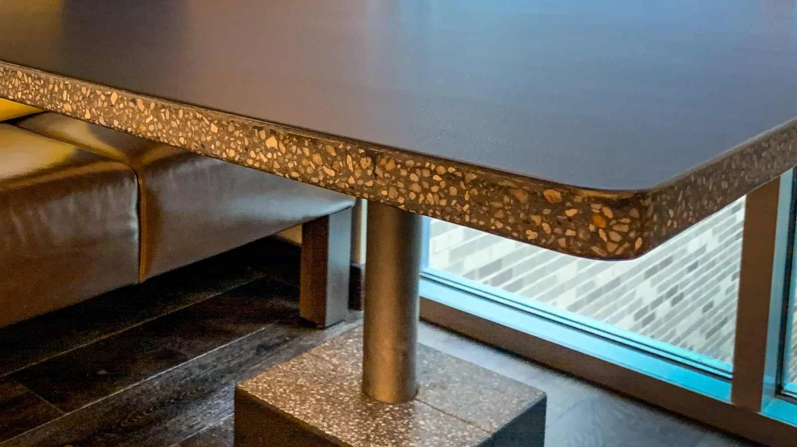 Close-up detail of a custom concrete table with exposed aggregate edge and rounded corner, designed and fabricated by The Concrete Anomaly for a commercial interior.