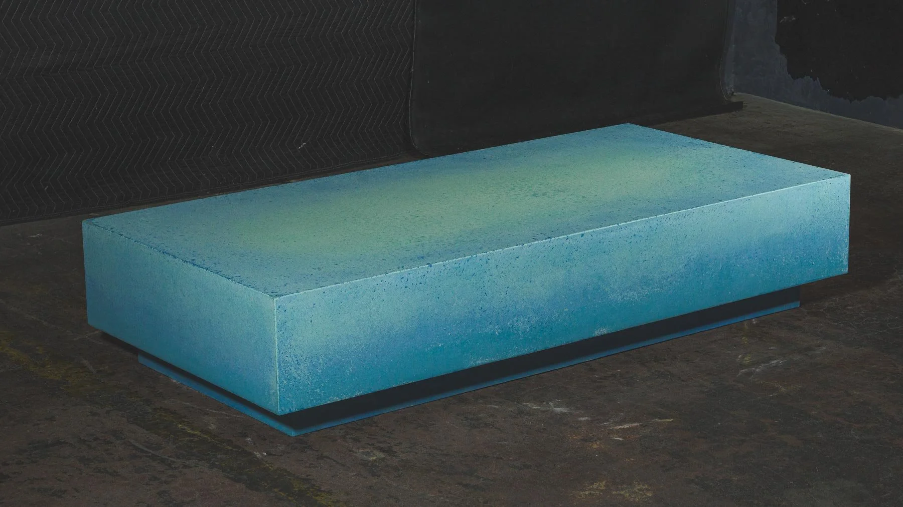 Turquoise concrete coffee table photographed in studio, highlighting layered mineral coloration and monolithic form.