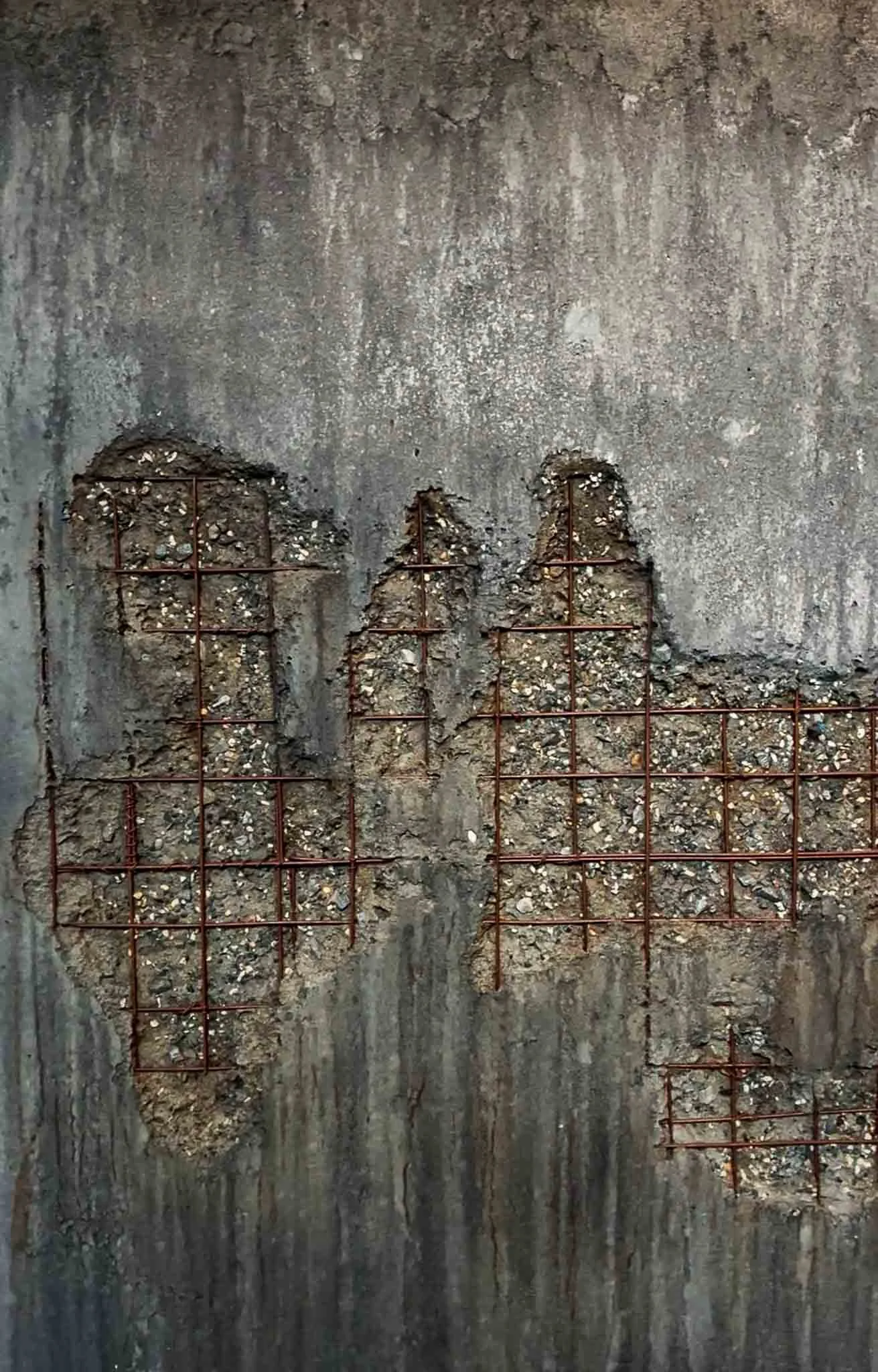 Close-up of a concrete wall with rough patches and exposed rebar in grid patterns, showing signs of renovation or damage.