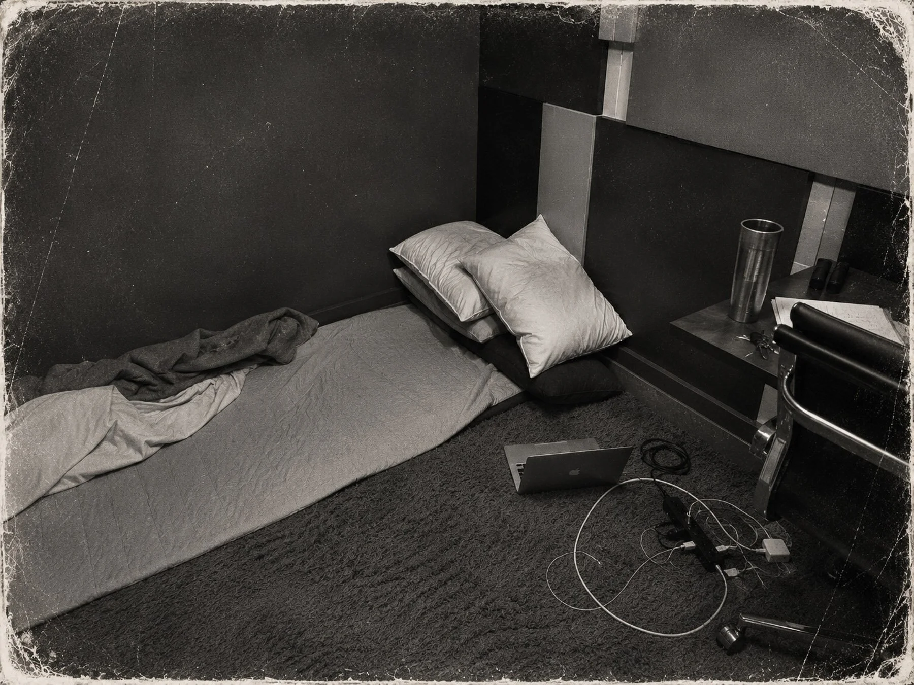 Monochrome archival-style photograph documenting an improvised sleeping space during the early development period of The Concrete Anomaly, featuring a floor mat, laptop, and isolated working environment.