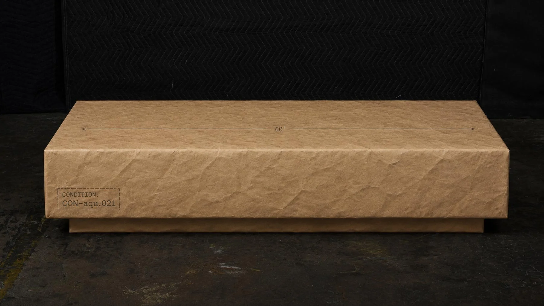 Paper-wrapped monolithic coffee table elevation with dimensional markings and condition CON-aqu.021 identification.