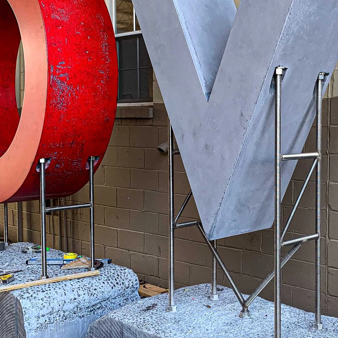 Red concrete letter O and gray letter V positioned on steel supports during fabrication of the monumental LOVE sculpture.
