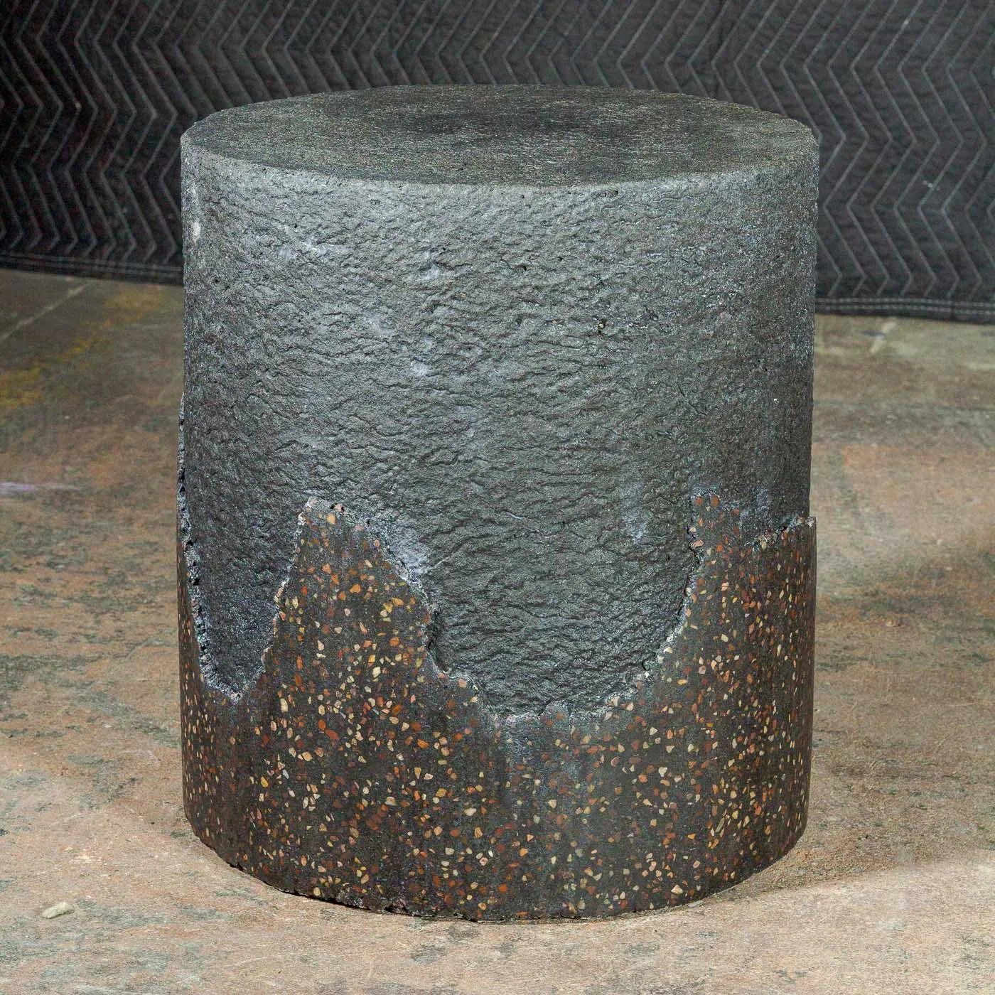 Hand-cast GFRC concrete cylinder with exposed terrazzo-inspired mineral aggregate and charred textured upper surface from The Concrete Anomaly.