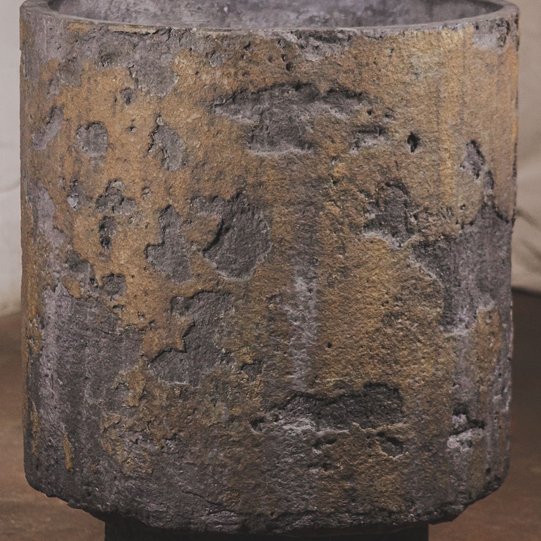 Macro surface detail of sculptural concrete vessel with layered erosion patterns and oxidized bronze-charcoal patina.