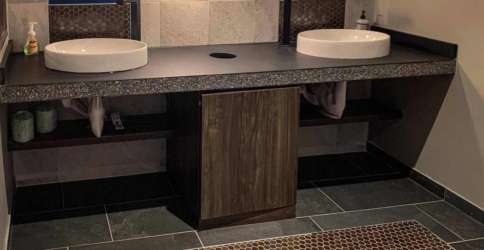 Custom double-sink concrete bathroom vanity top with honed aggregate surface, fabricated by The Concrete Anomaly for a commercial restroom installation.
