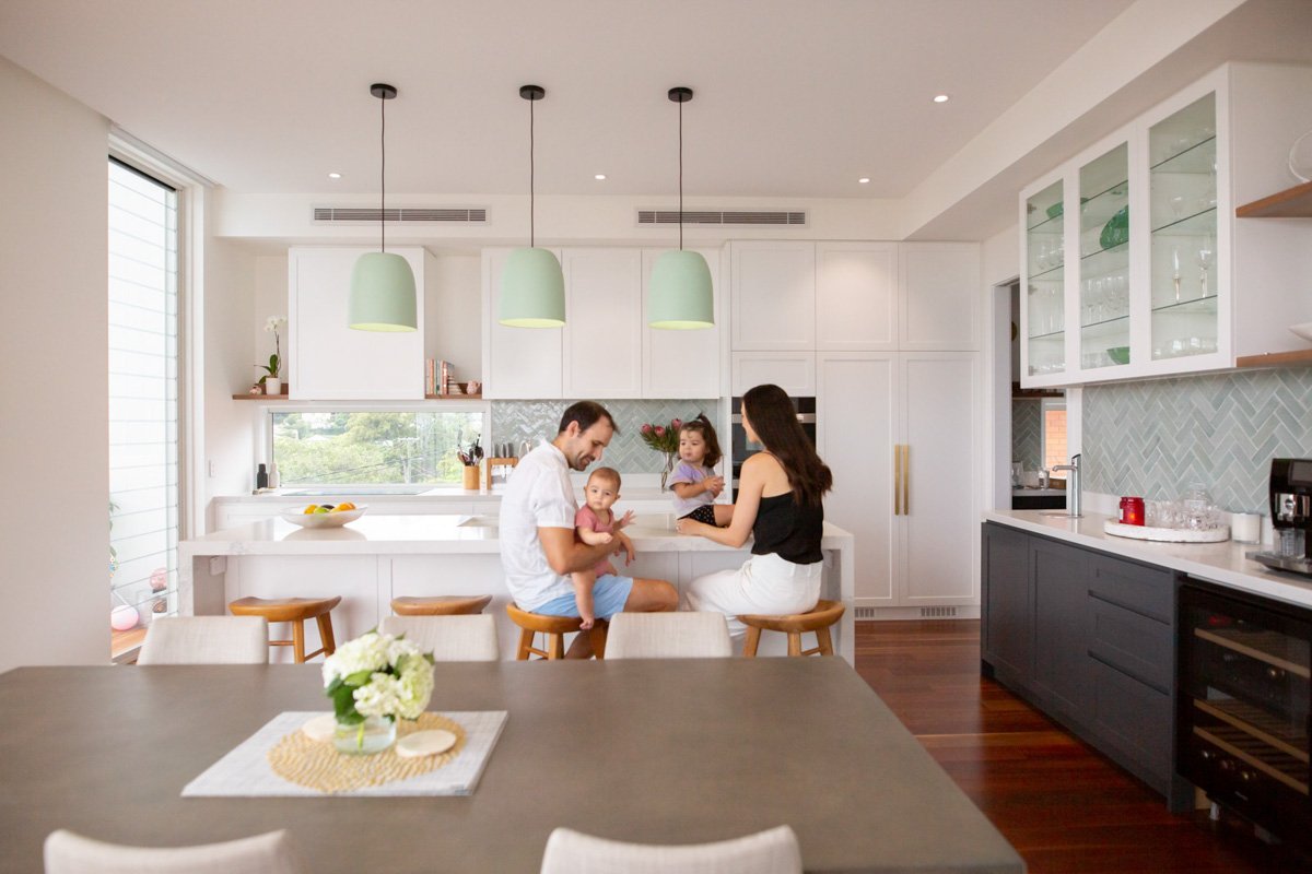 Family of four with two young children sitting at a kitchen island in a modern, bright kitchen.