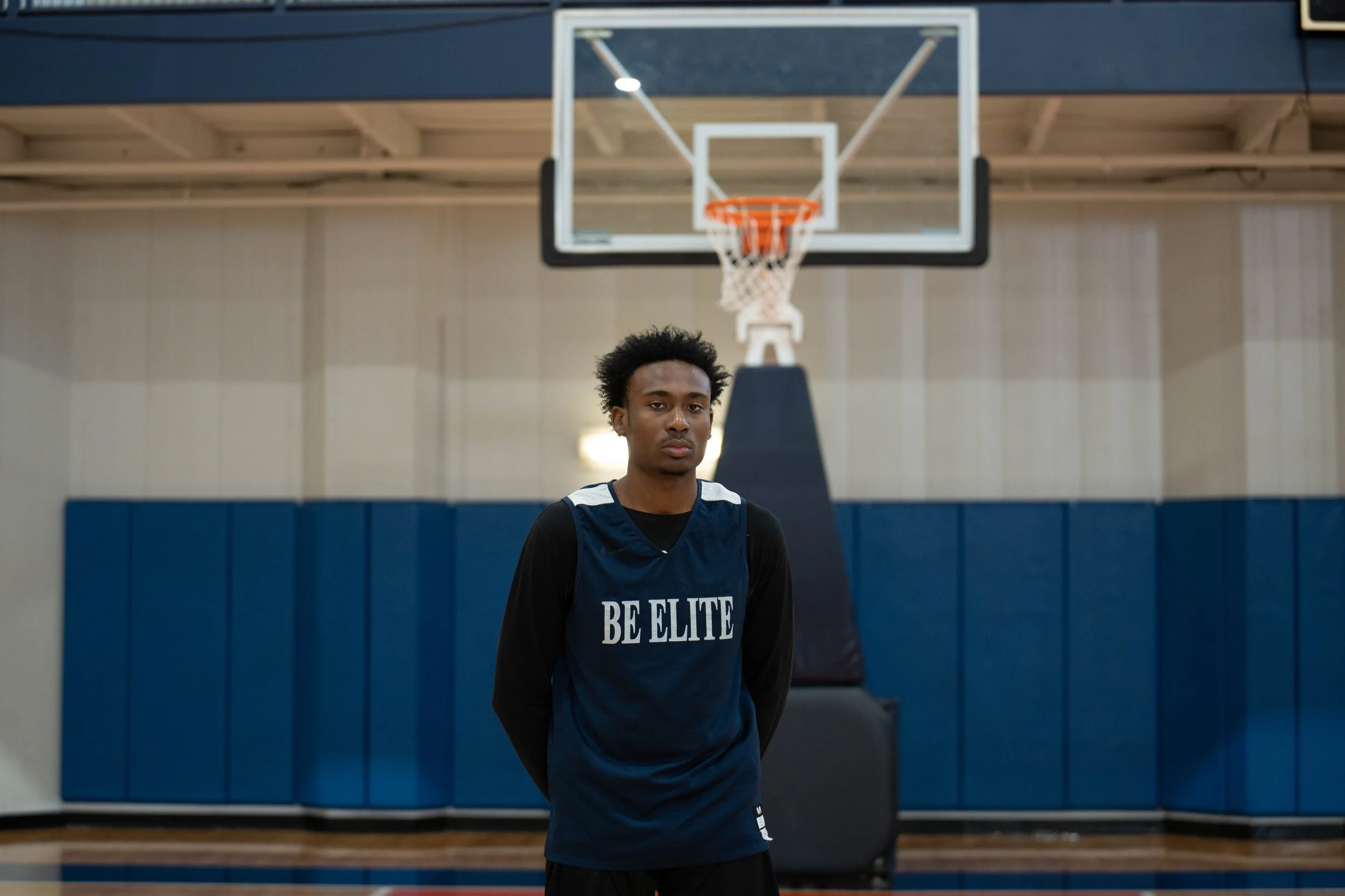 Basketball player wearing a jersey with 'Be Elite' in a gym.