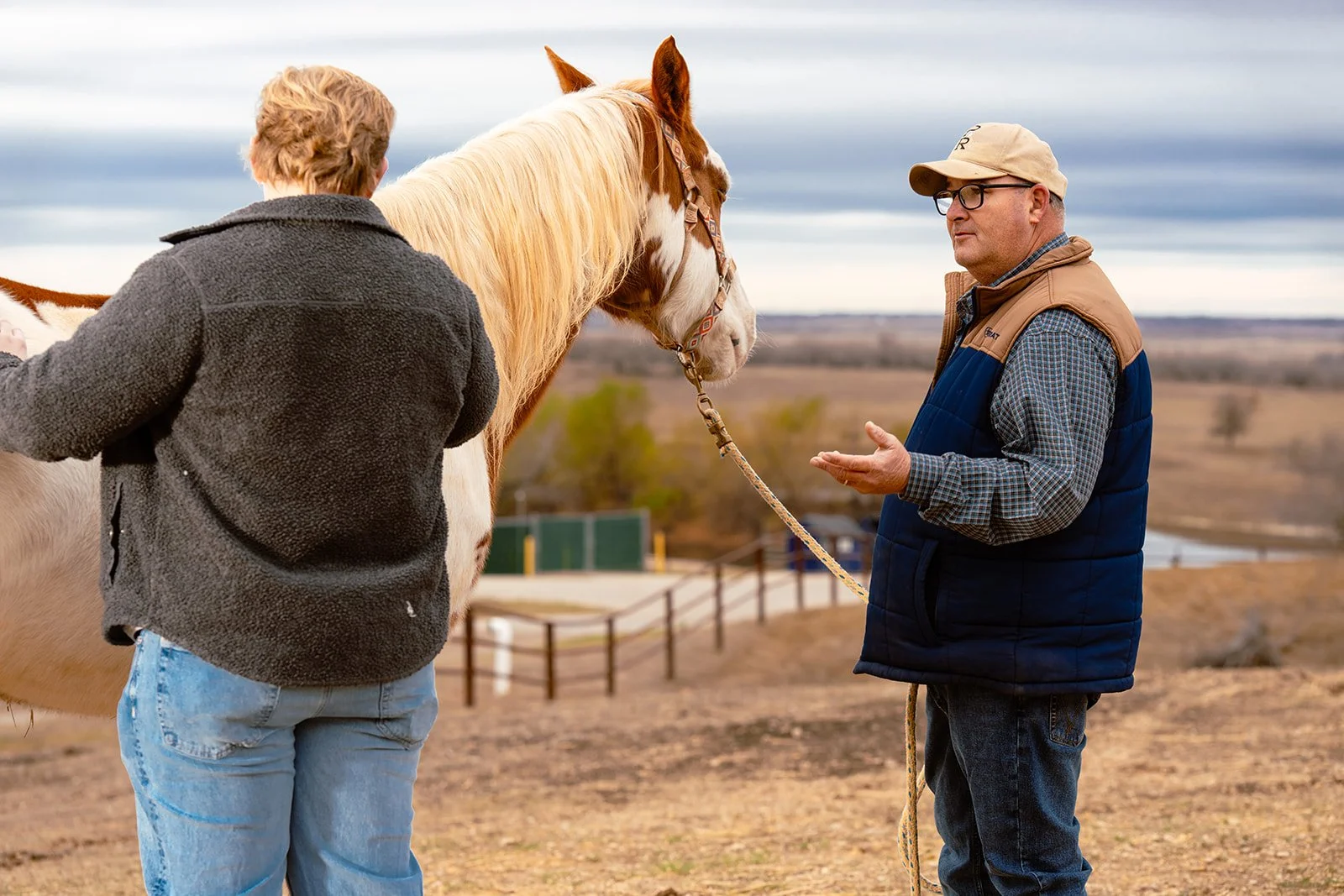 Man holding horse reins while talking on a ranch.
