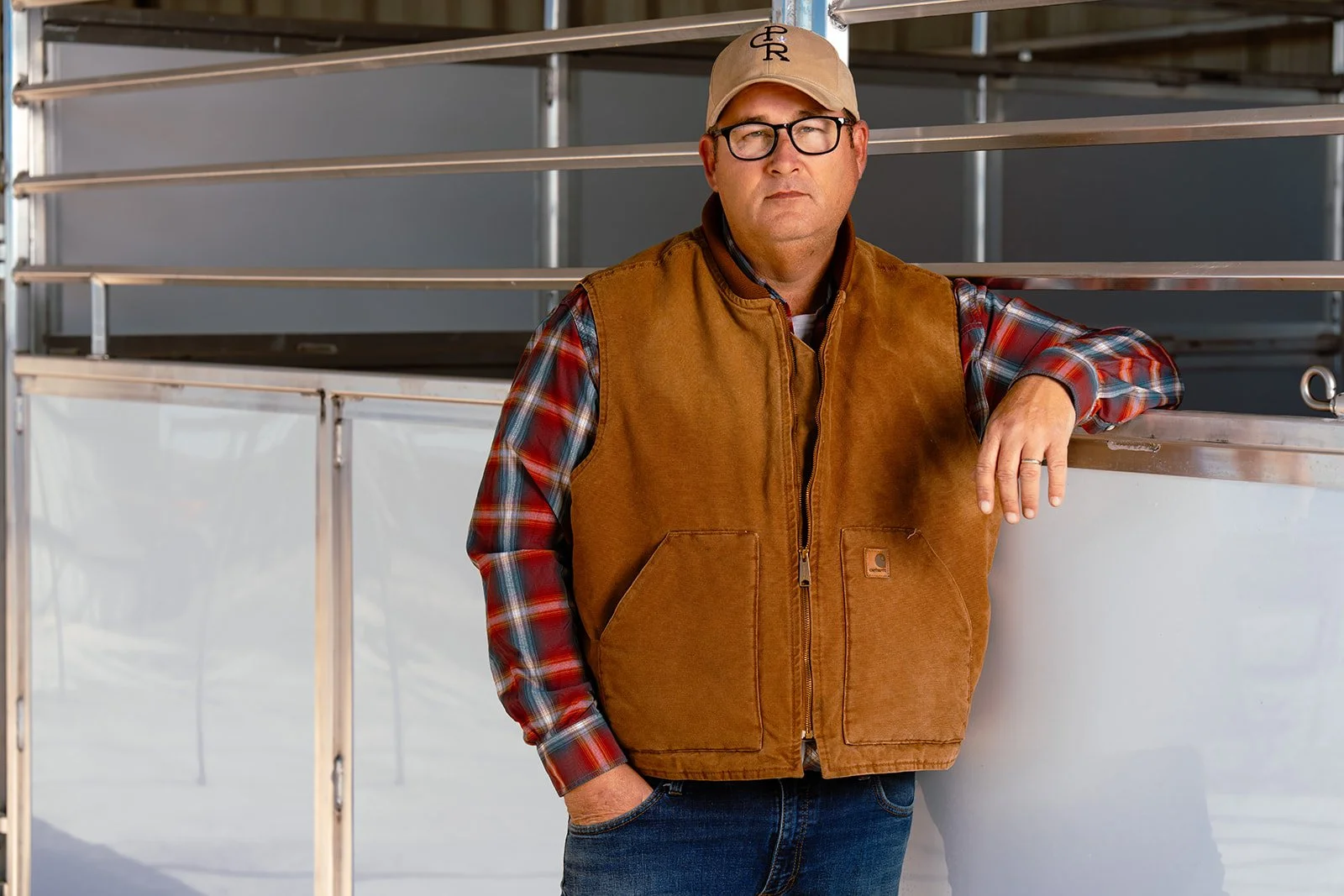 Man in vest and baseball cap beside horse stalls