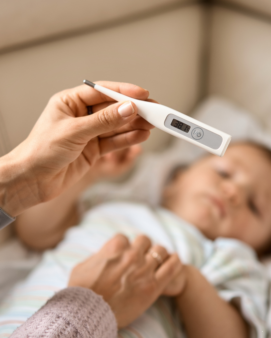 Parent checking baby’s temperature with digital thermometer showing fever of 38.1°C. Sick infant lying in bed during illness, home healthcare and fever monitoring concept