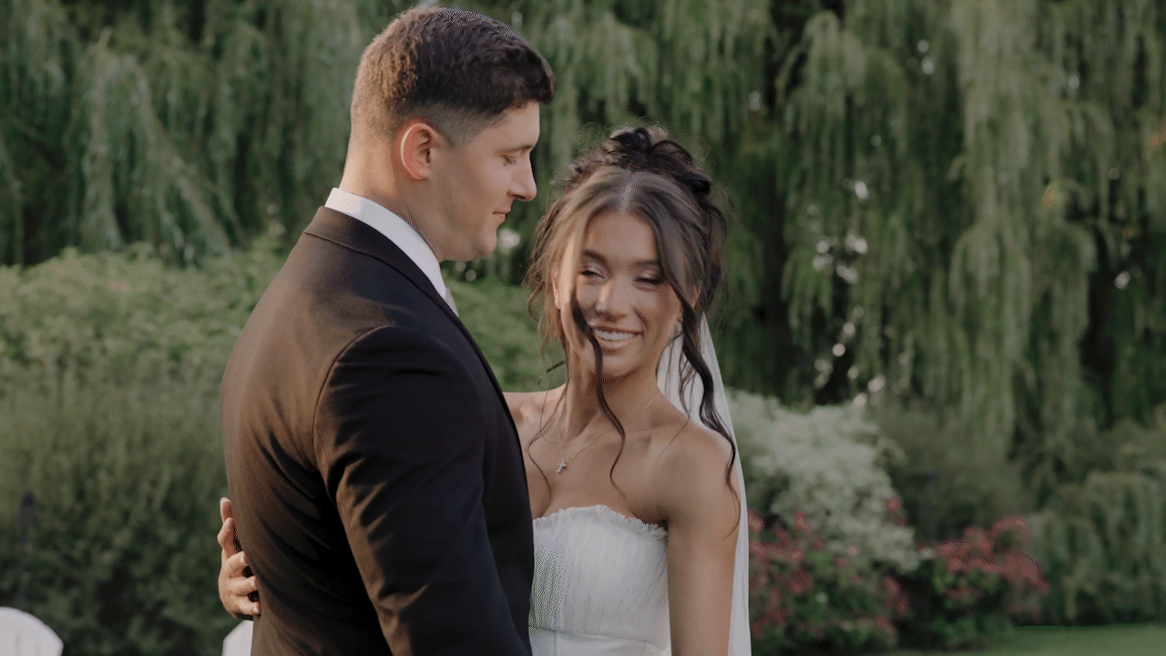 A bride and groom share a romantic moment outdoors, with greenery and trees in the background.