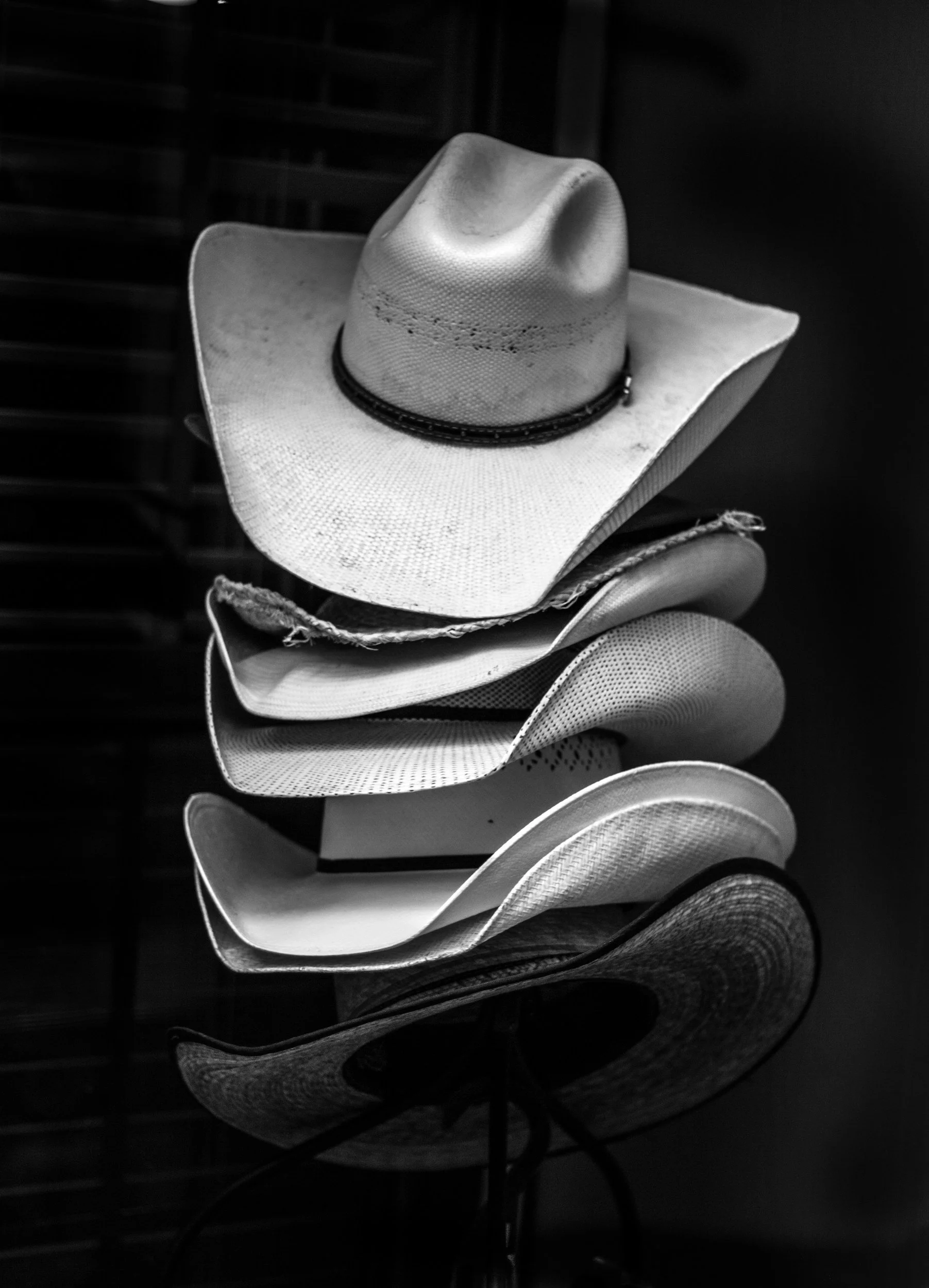 A stack of various cowboy hats, with a straw cowboy hat on top, in black and white.