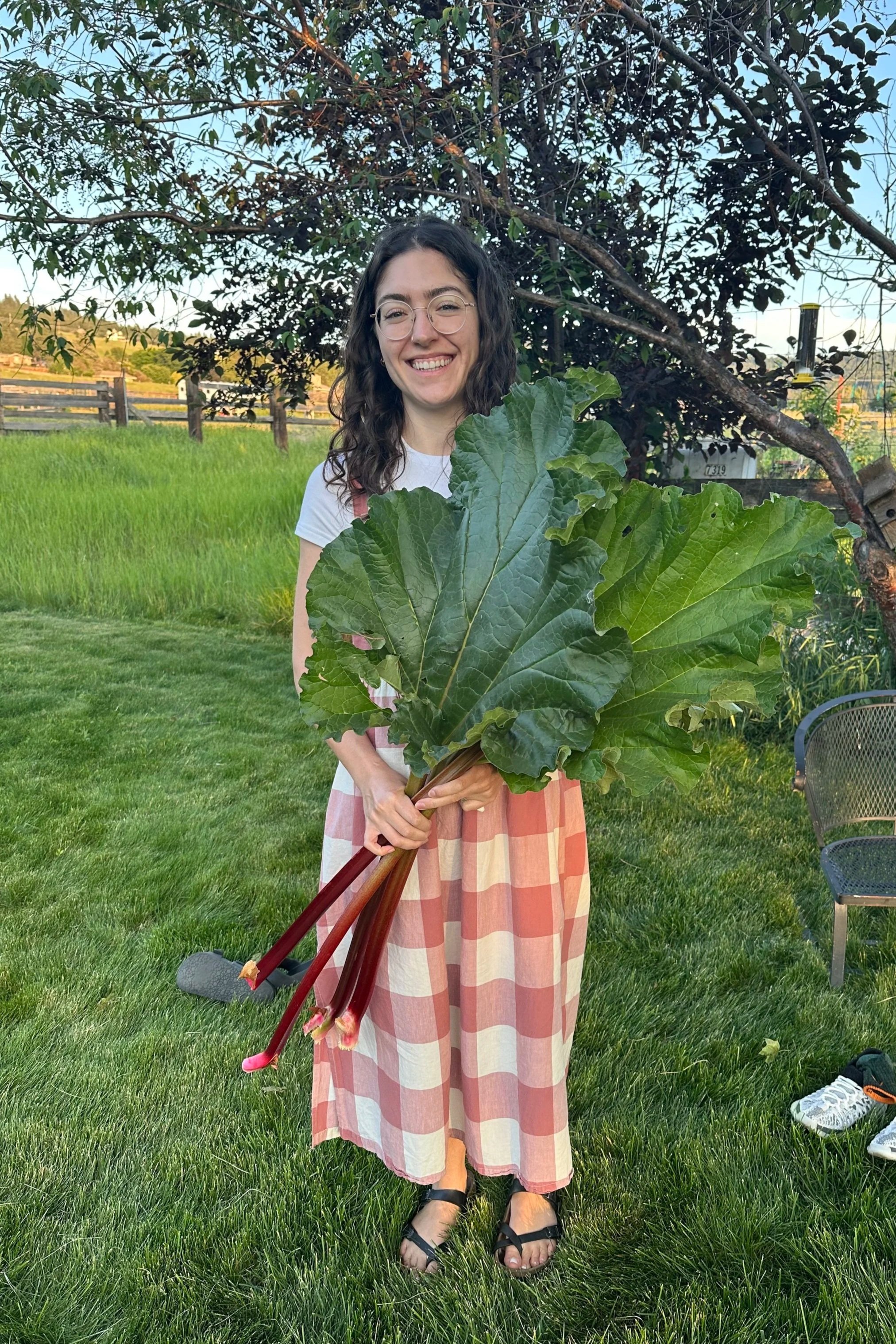 Maria Taylor, registered dietitian nutritionist, holding large stalks of rhubarb, smiling at the camera.