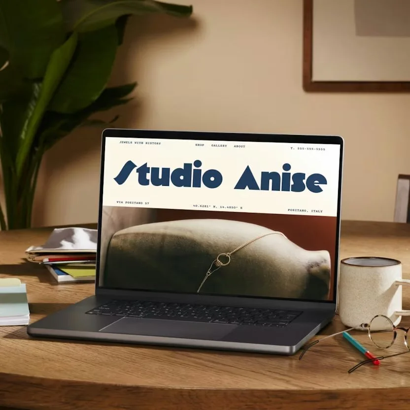 Photo of a laptop on wooden desk displaying 'Studio Anise' website with jewelry image.