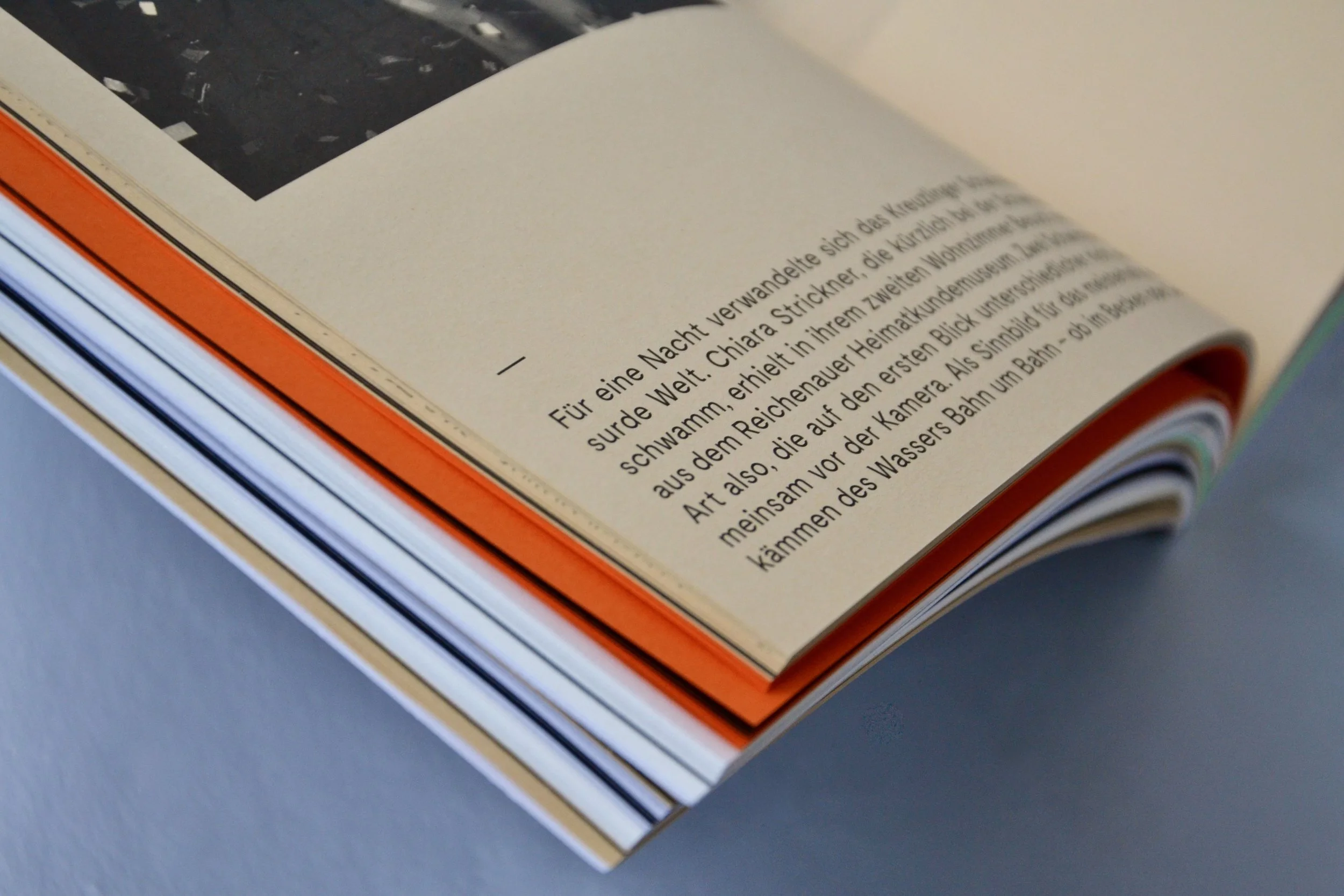 Offenes Buch mit Textseite und farbigen Seiten im Inneren, Text in deutscher Sprache, auf glattem grauem Hintergrund