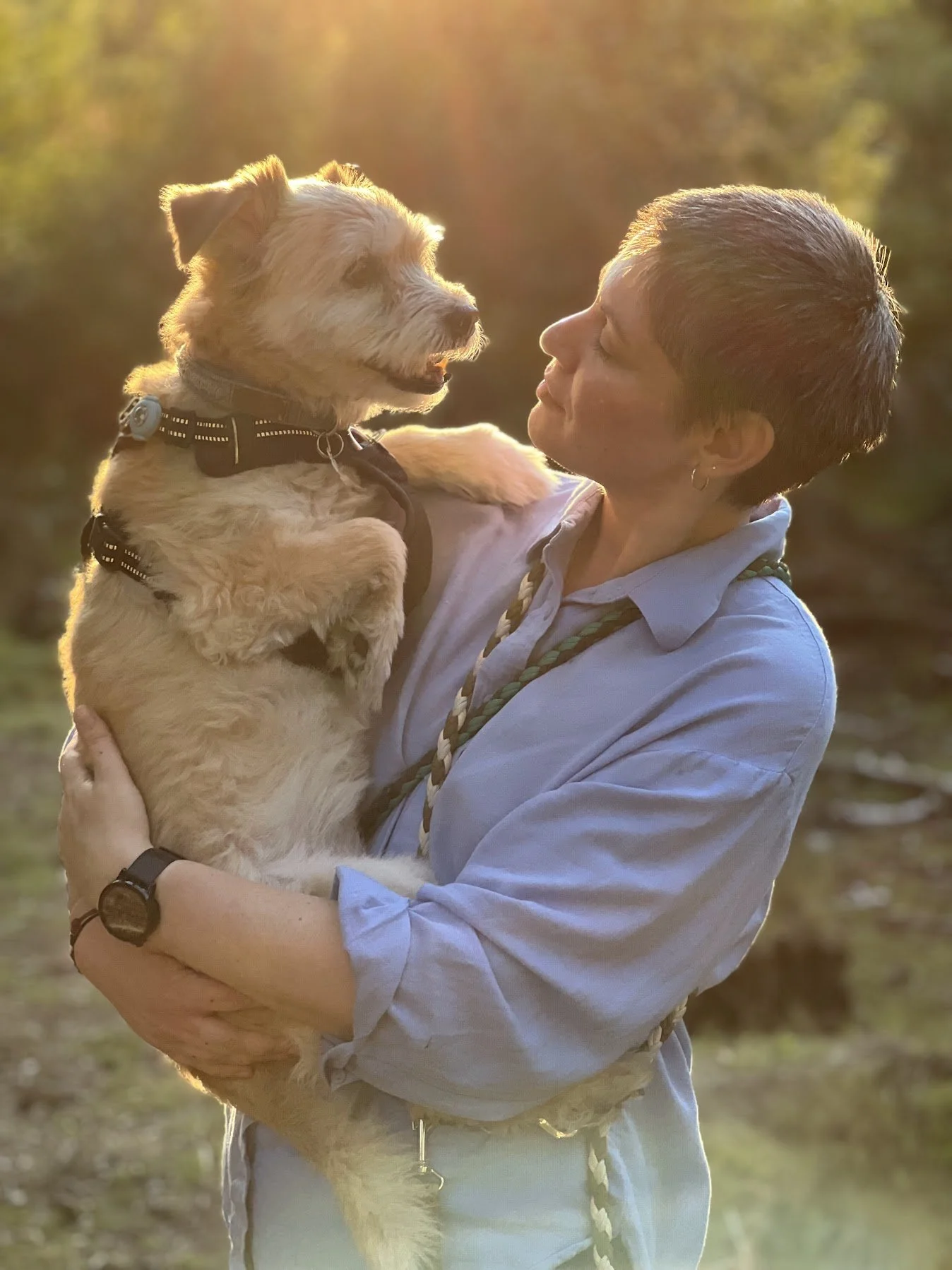 Plenerowy portret kobiety trzymającej małego psa w ciepłym świetle zachodu słońca, patrzą na siebie