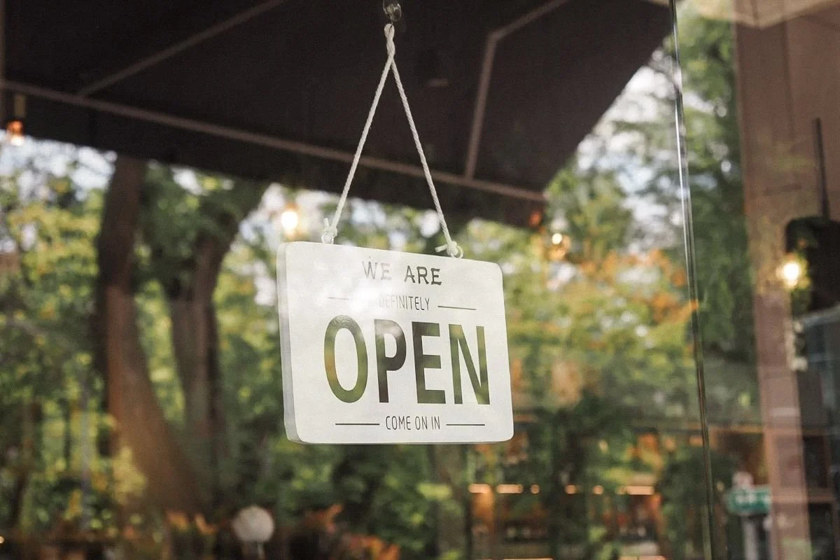 Open” sign hanging on a local business window, symbolizing renewed visibility and community presence