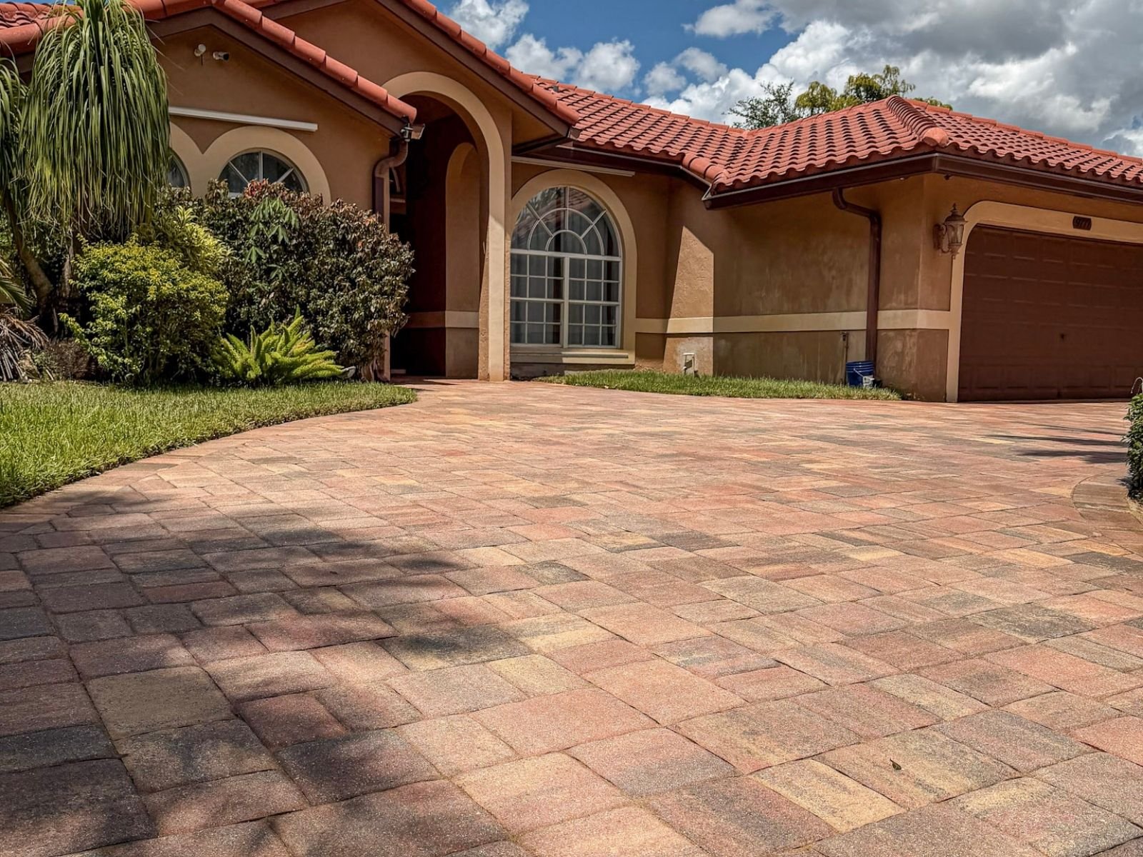 Residential brick paver driveway in Coral Springs before cleaning and sealing, showing weeds between joints and uneven surface color.