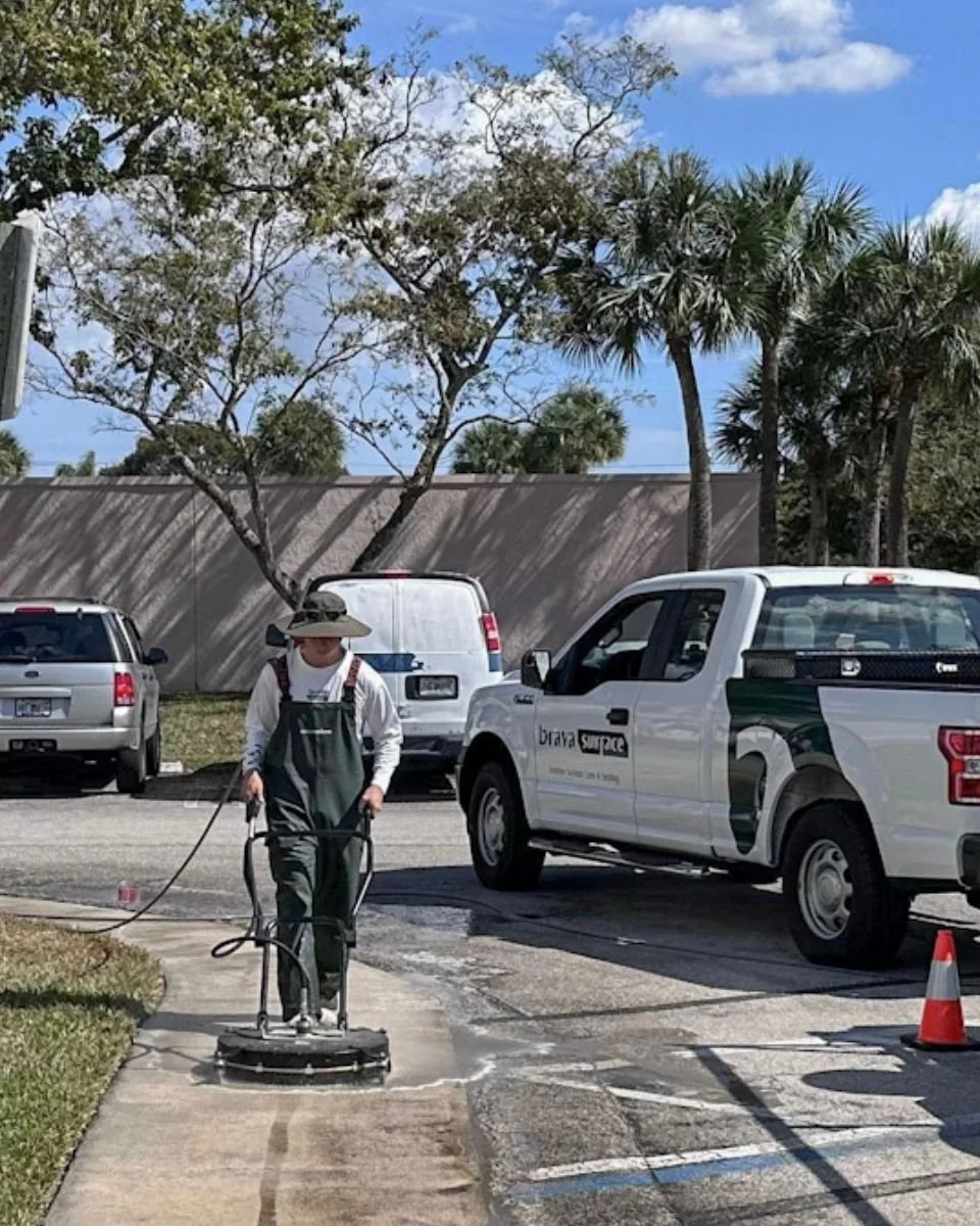 BravaSurface technician cleaning a concrete walkway with a surface cleaner beside the company's branded truck.