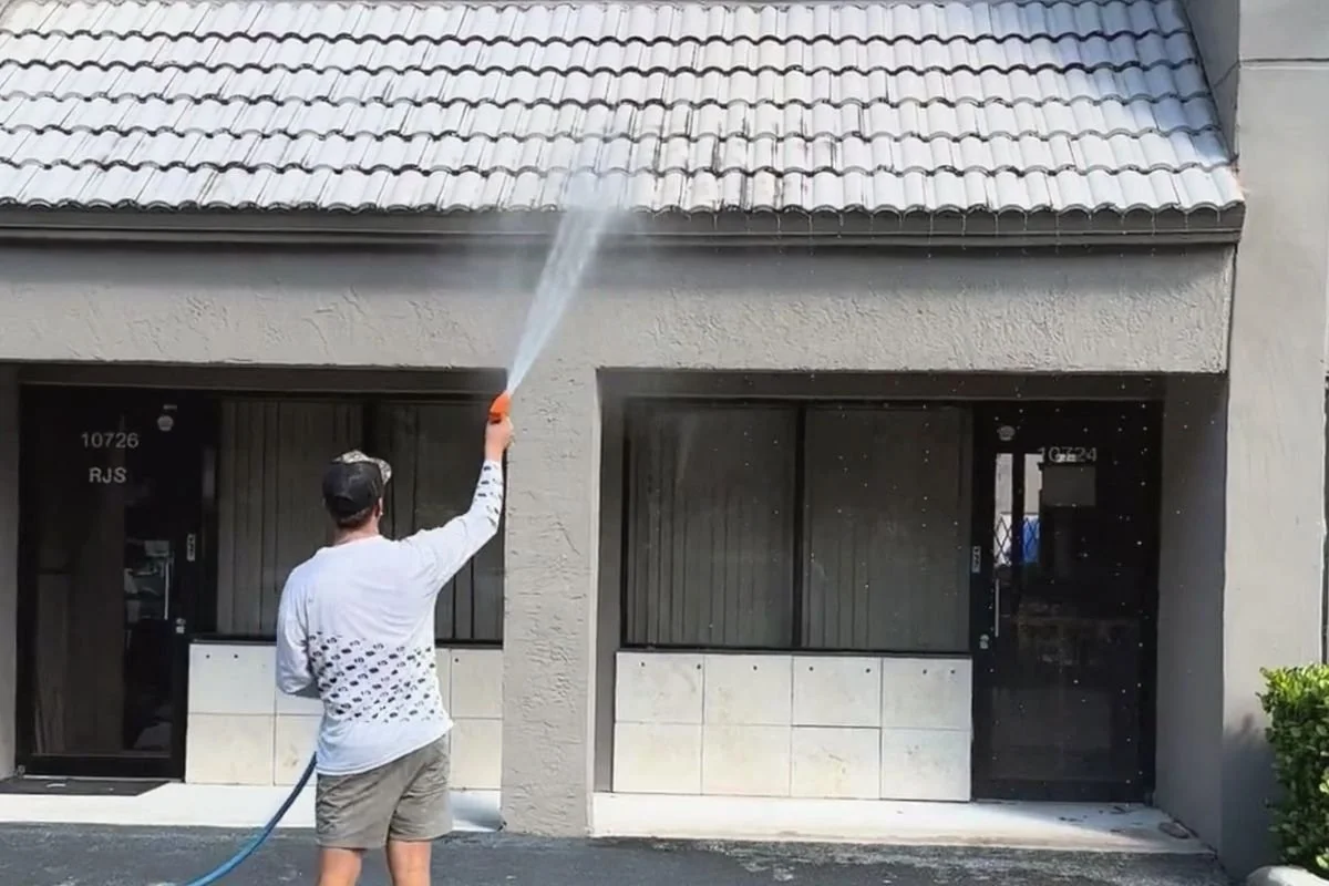 Technician soft washing a tile awning above commercial storefronts in Sunrise, Florida.