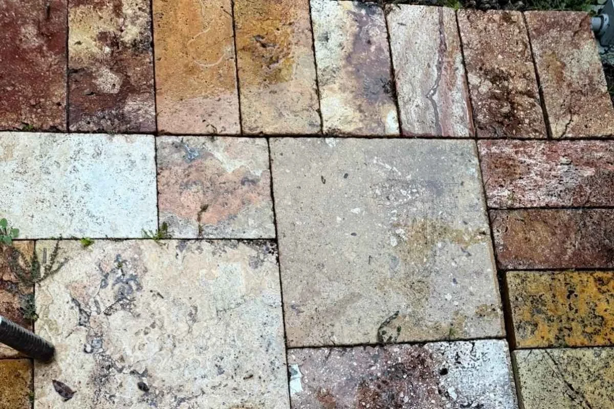 Travertine patio joints with buildup and weeds before cleaning and sealing.