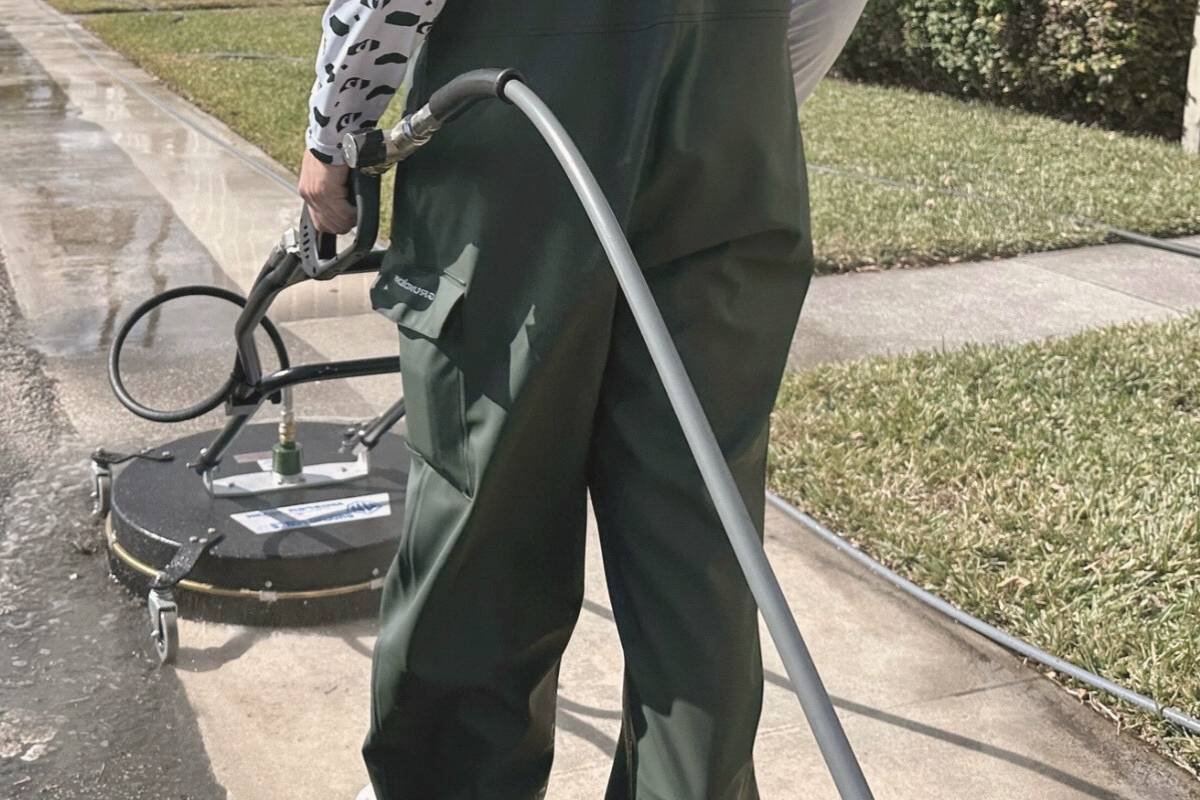 Technician pressure washing a concrete walkway in Coral Springs with algae and moisture that can make the surface slippery.